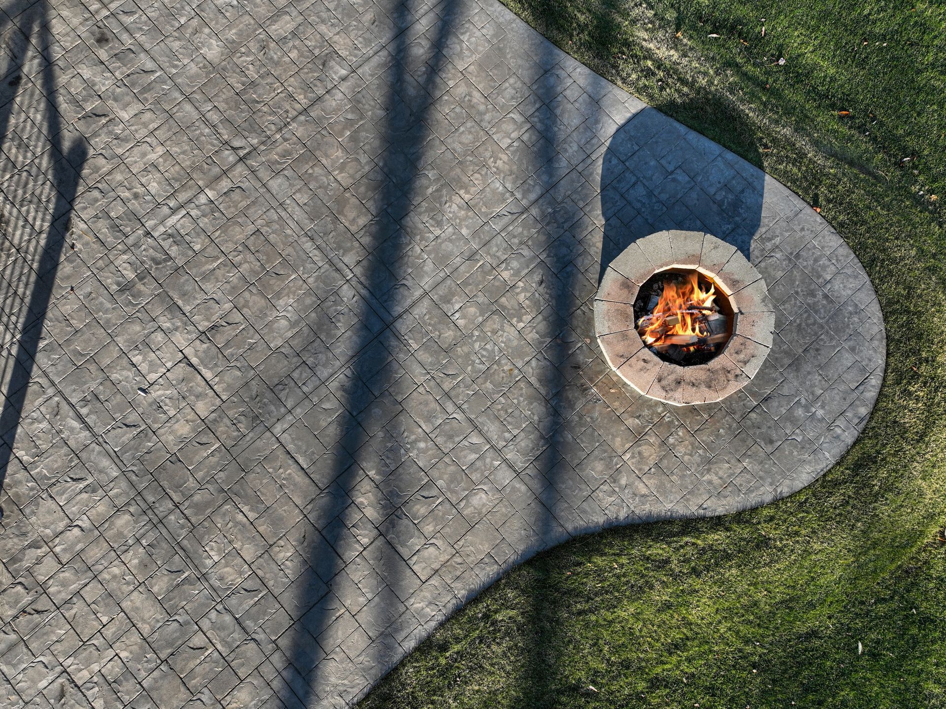 Overhead view of a gray brick patio with a burning fire pit and grassy area.