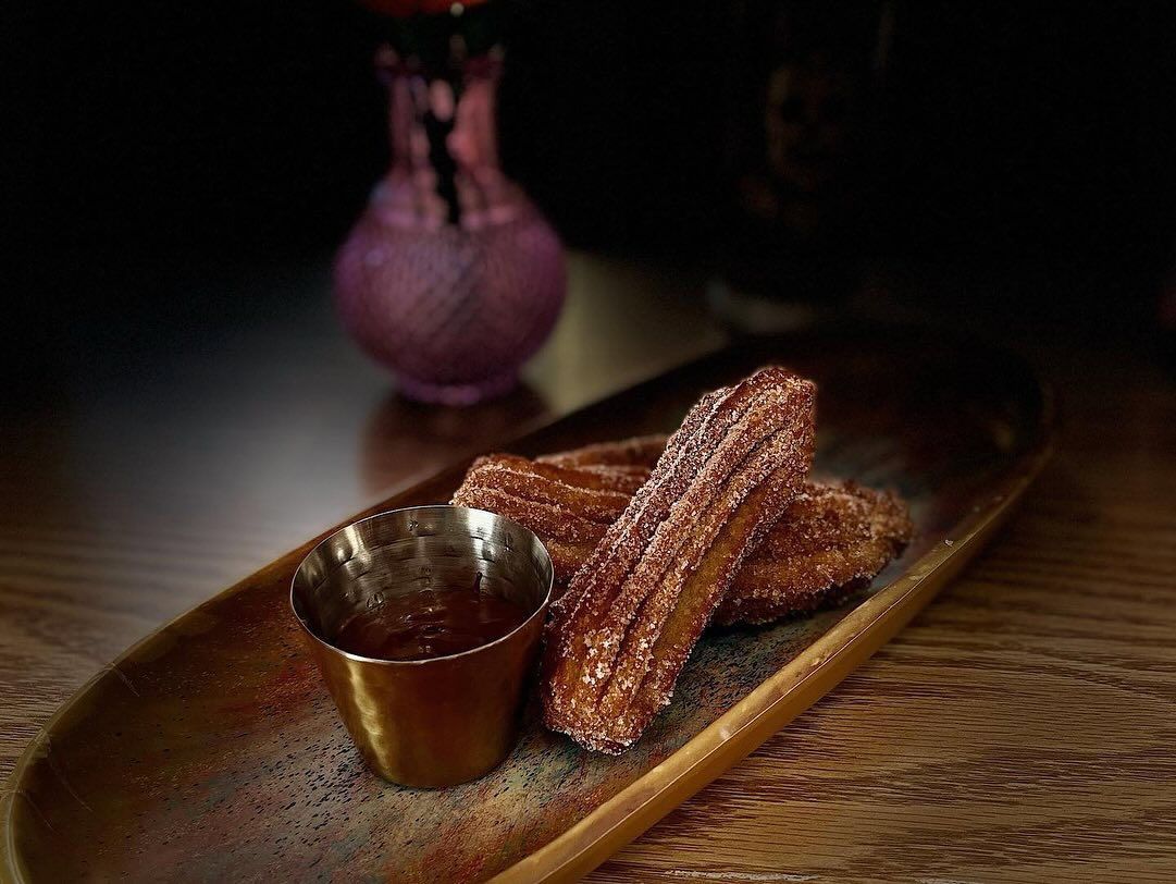 A wooden plate topped with churros and a cup of dipping sauce.
