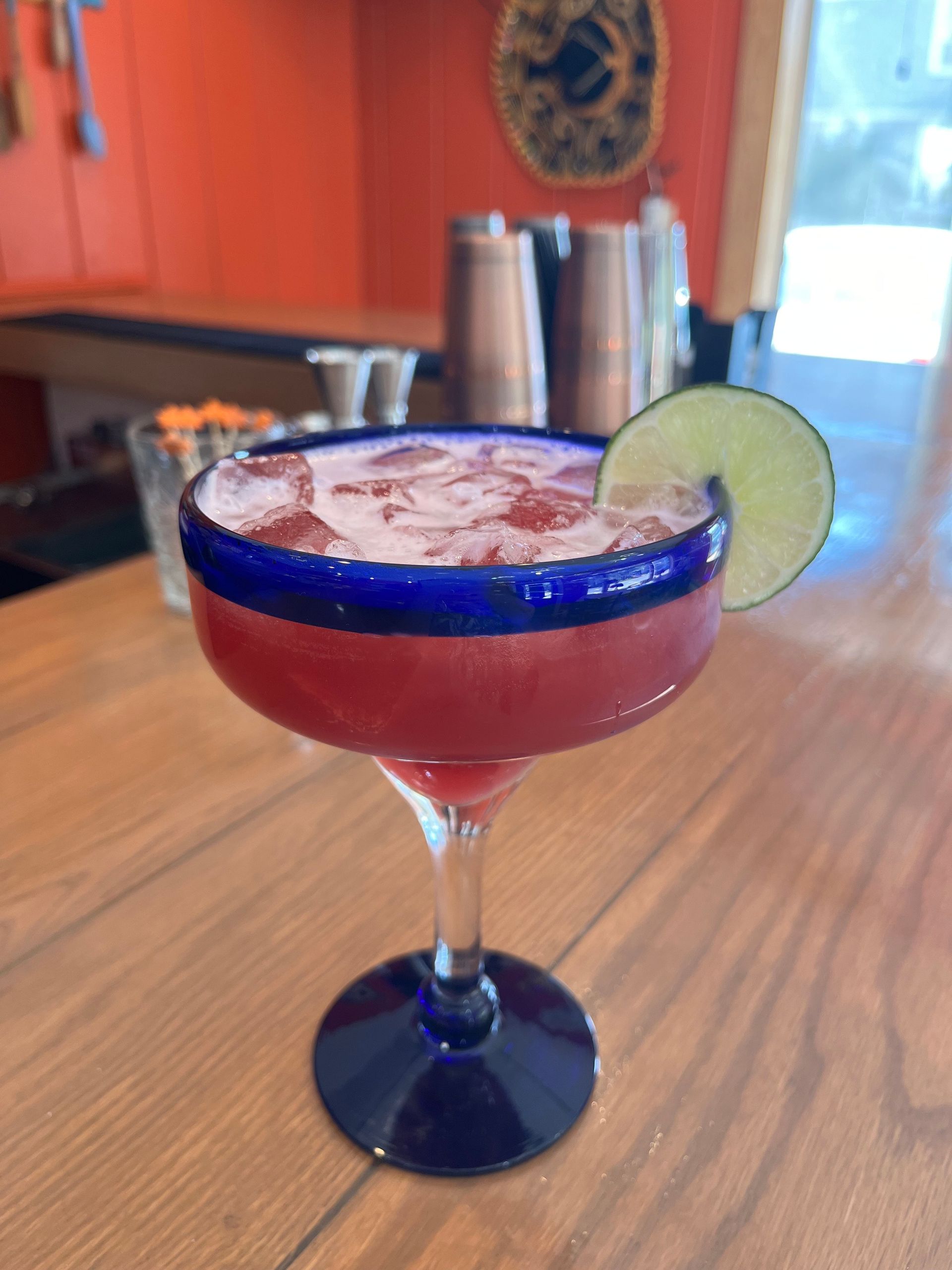 A strawberry margarita with a lime wedge on a wooden table.