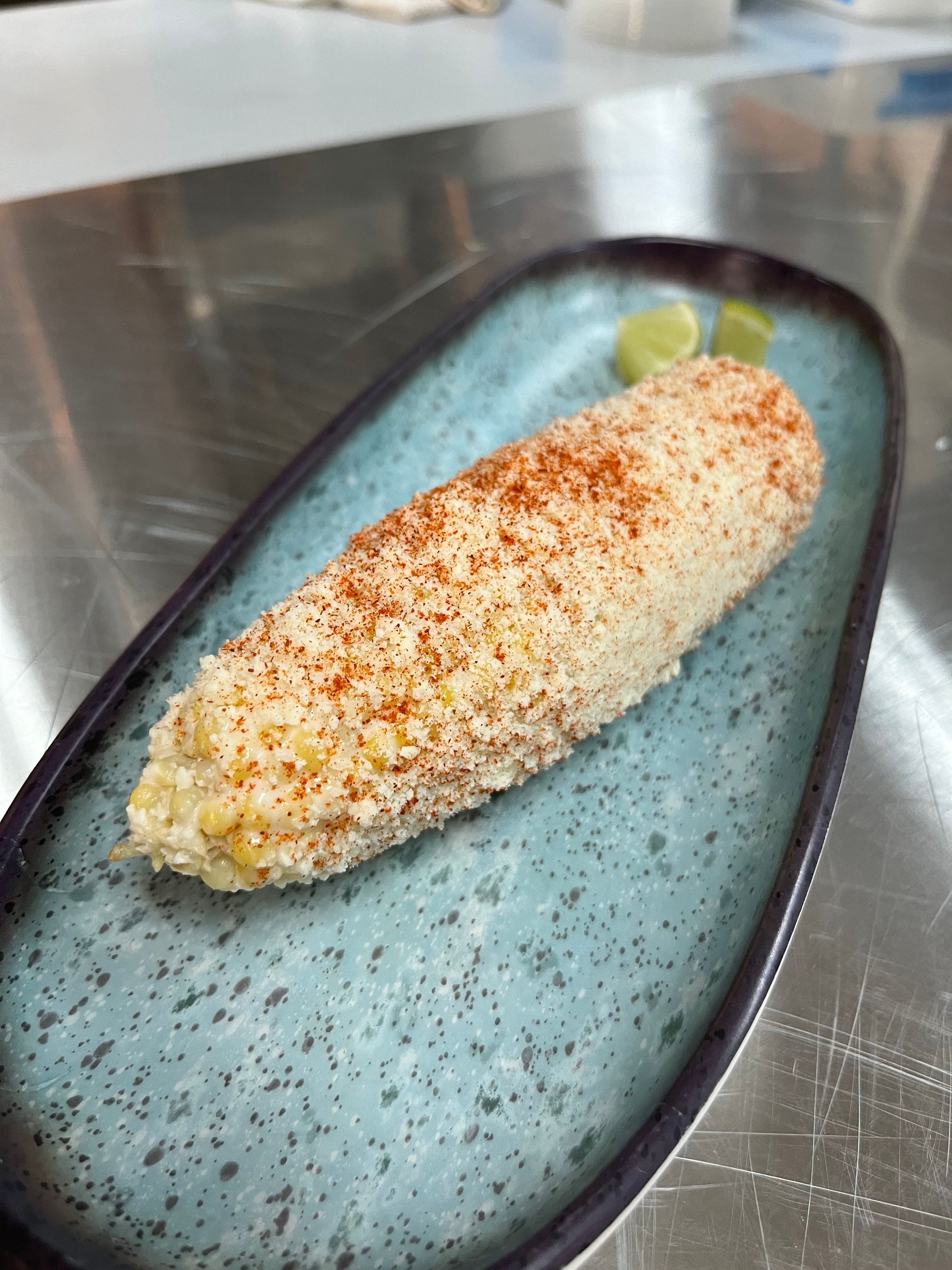 A close up of a corn on the cob on a blue plate on a table.