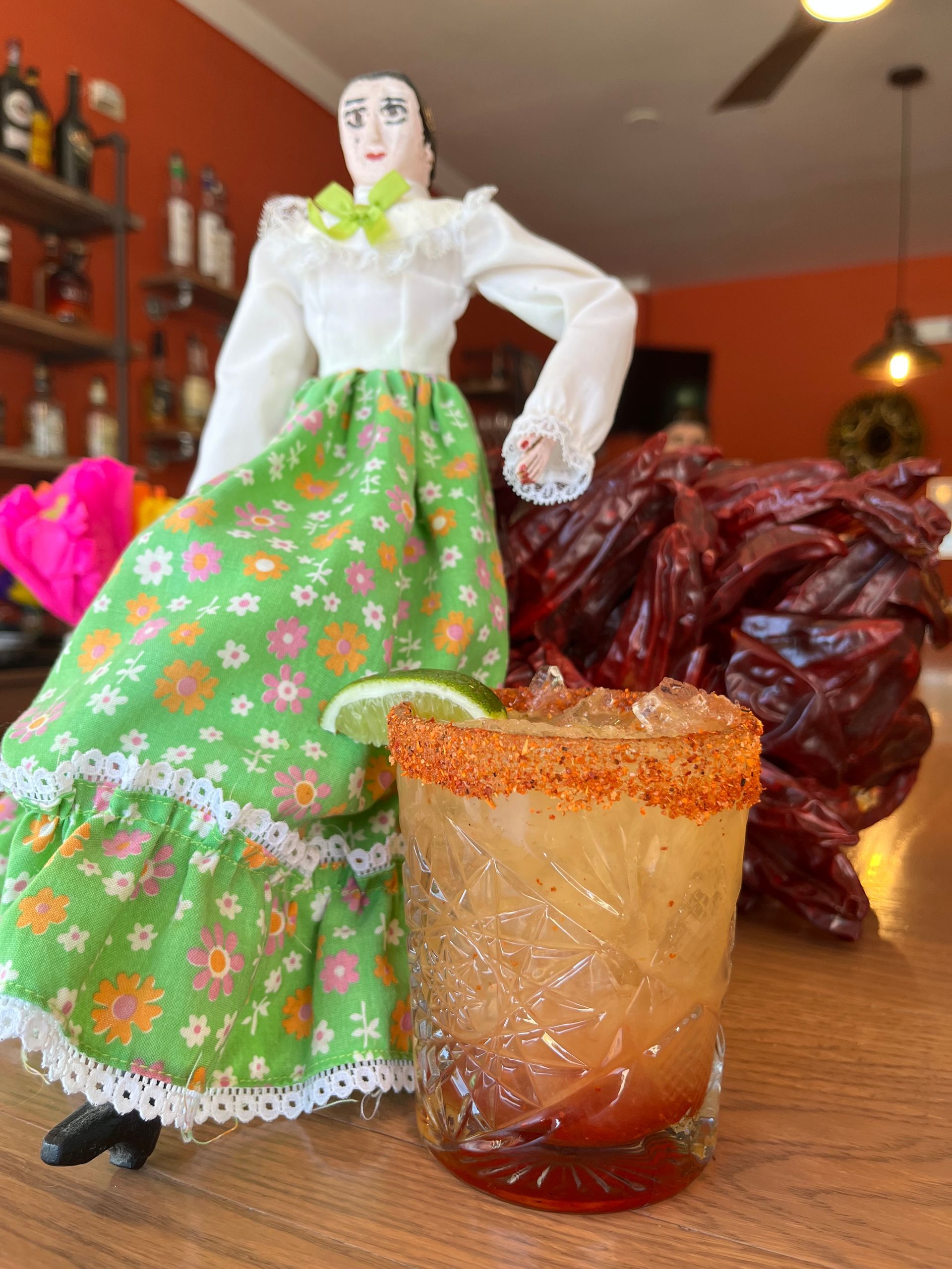 A doll in a green dress is standing next to a drink on a table.