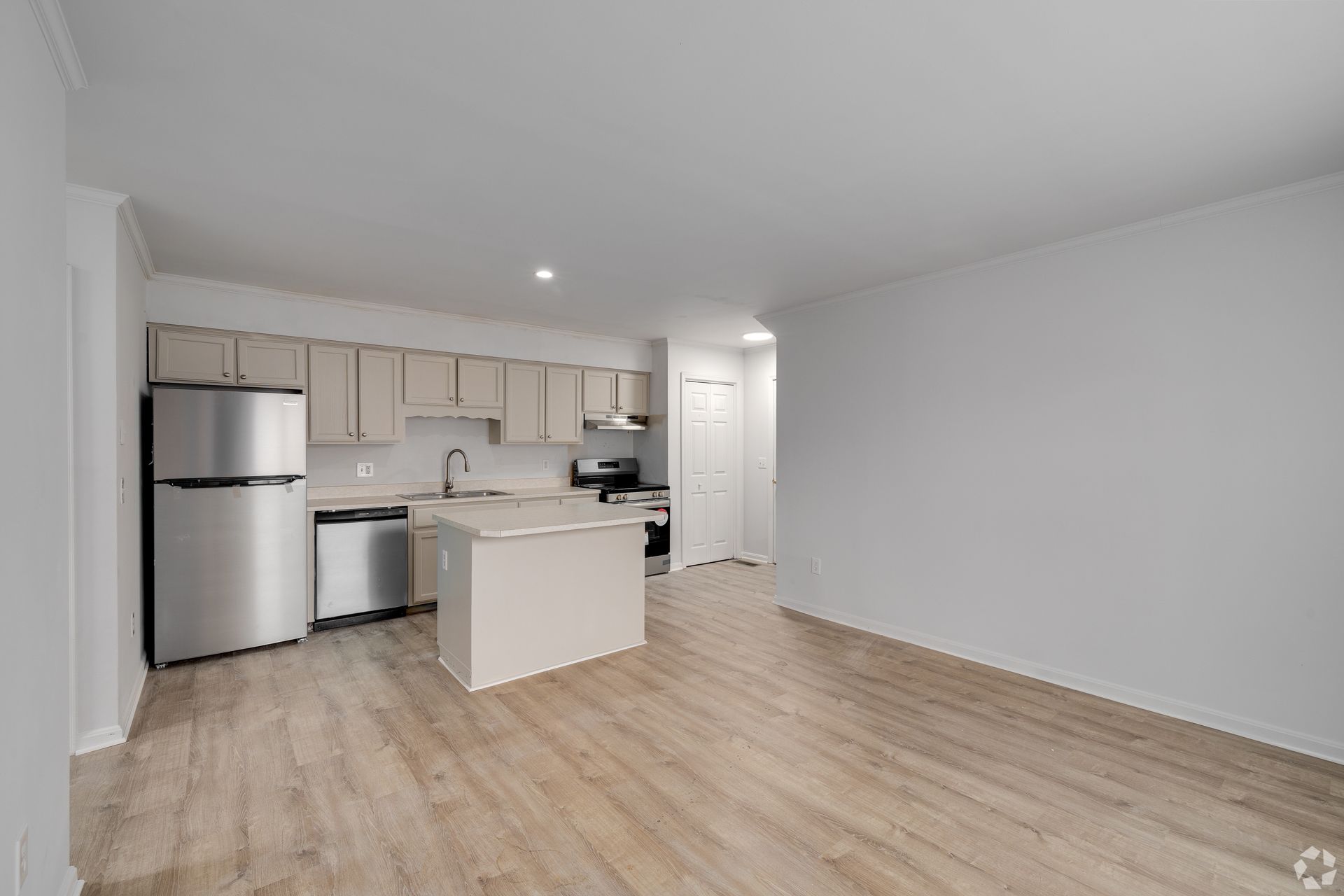 Open-plan kitchen and living space, featuring stainless steel appliances, light cabinets, and wood-look flooring.
