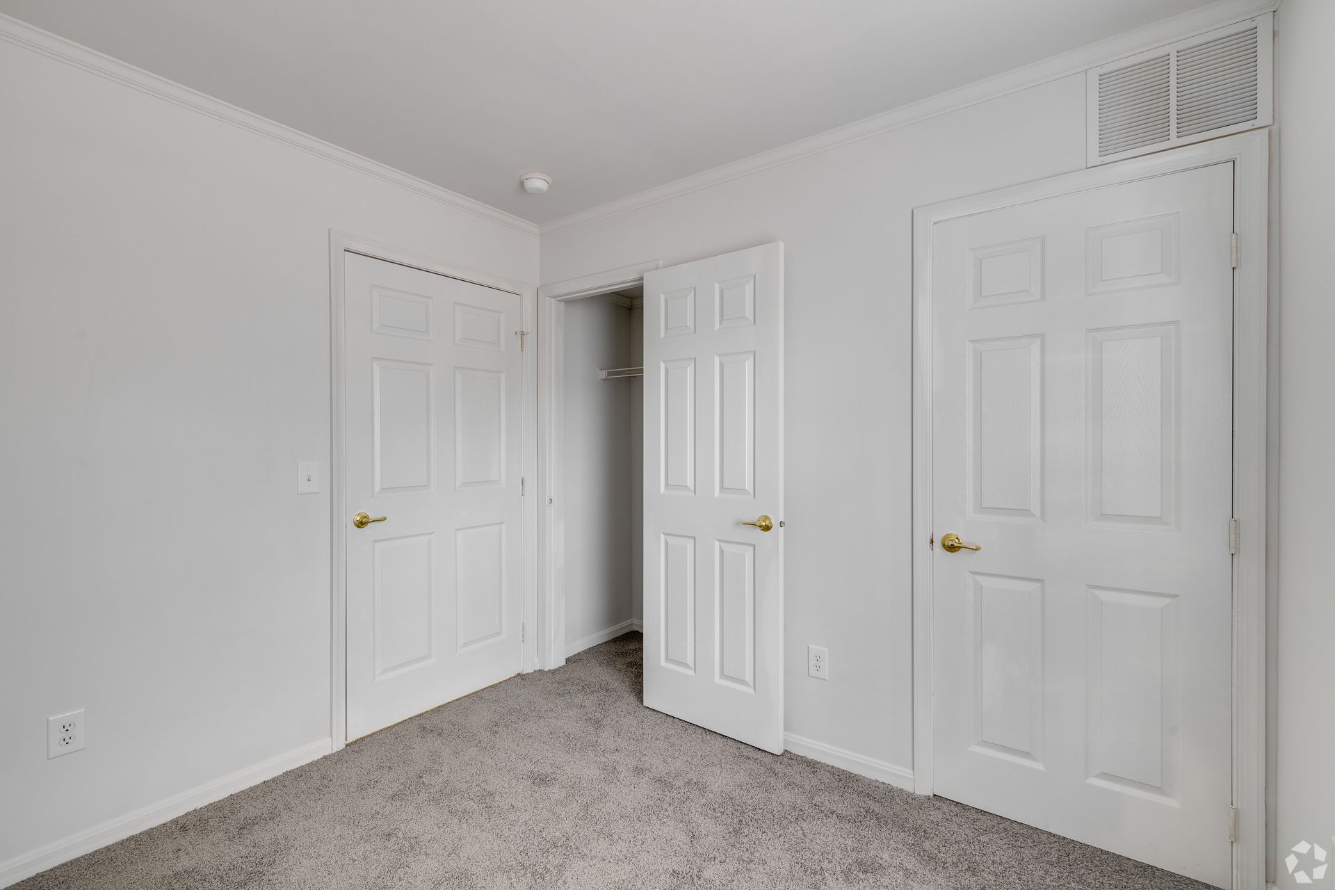 Empty room with three white doors, one open revealing a closet, and gray carpet.