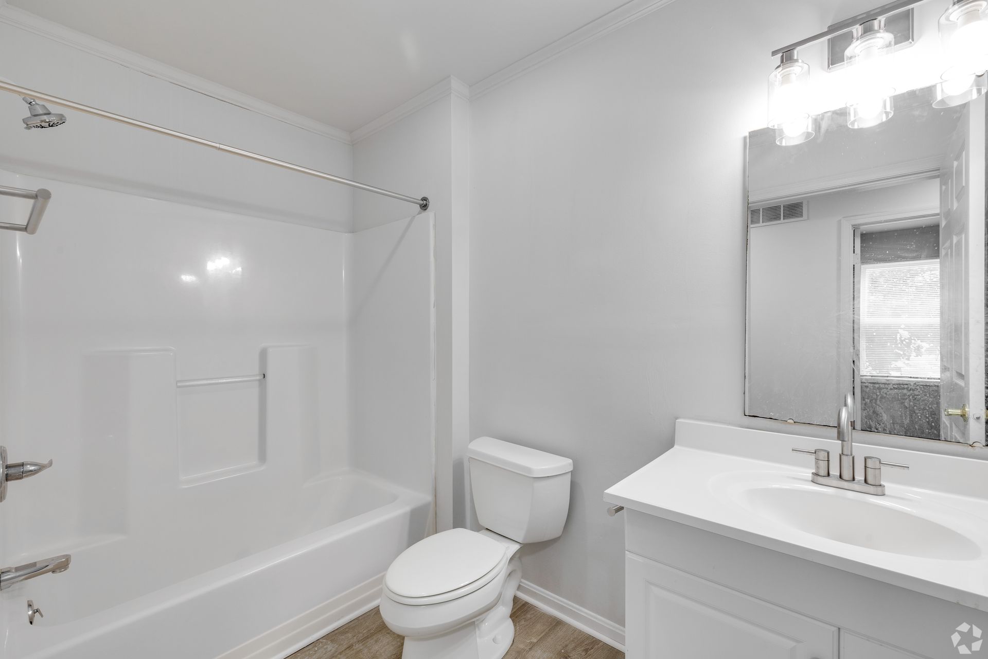 Bathroom with white tub, toilet, and vanity. Gray walls and wood-look floor.