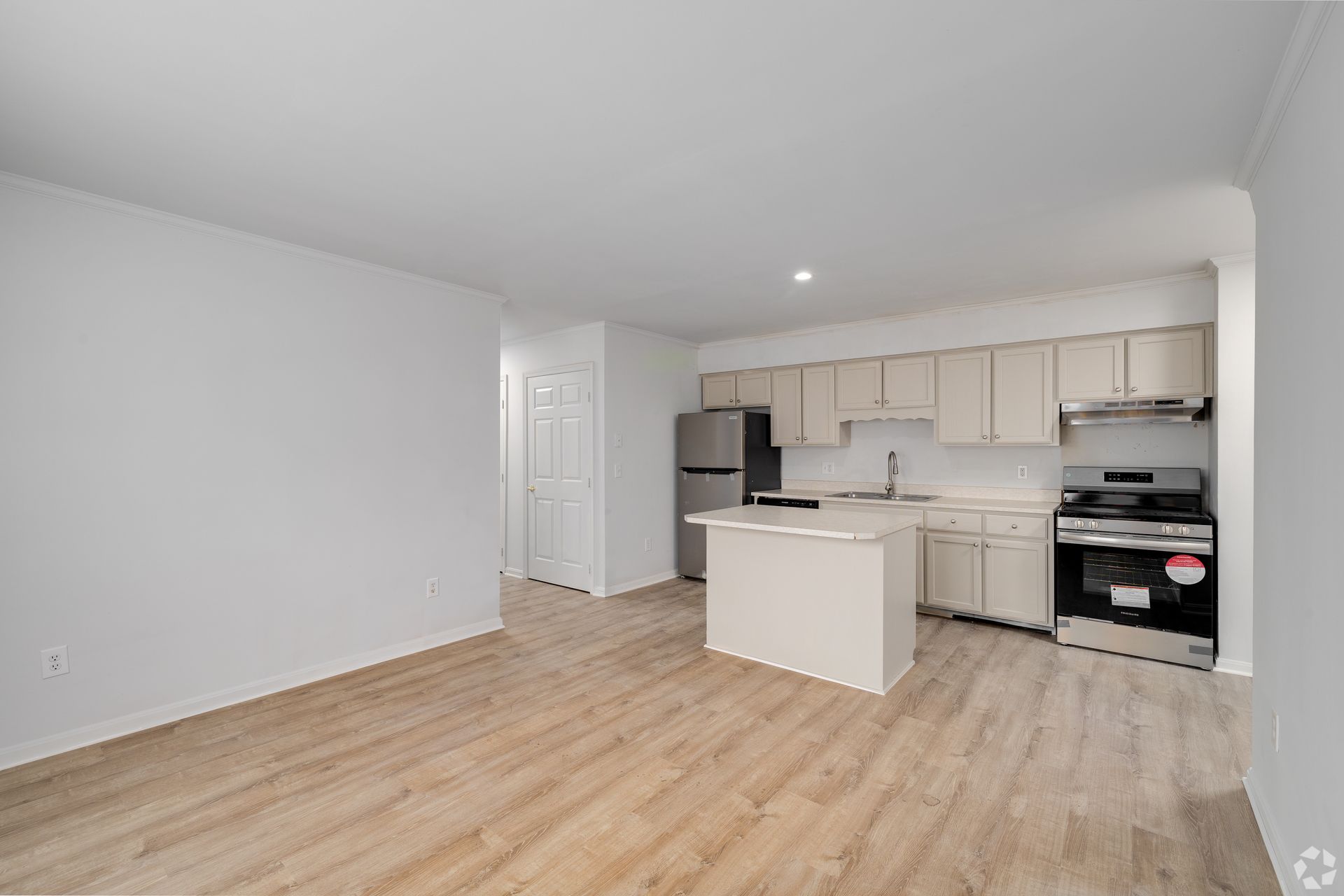Empty, modern apartment with kitchen and island. Light wood floors, light-colored cabinets, stainless steel appliances.