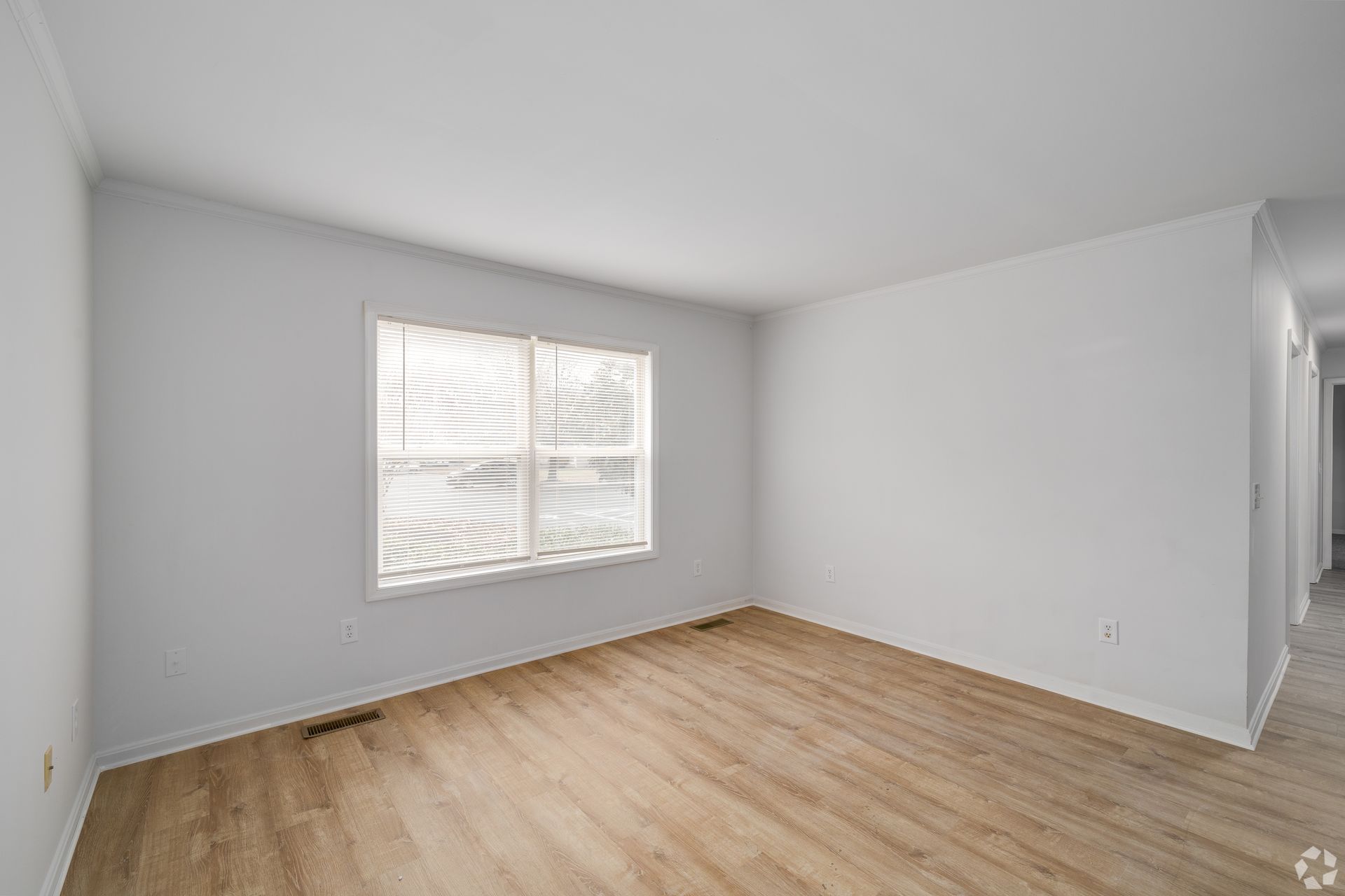 Empty room with wood-look floor, window with blinds, and white walls.