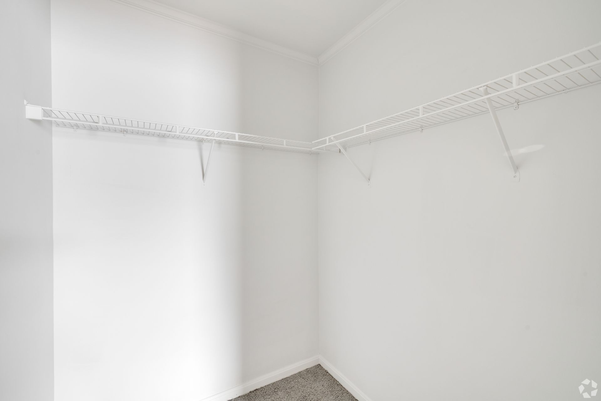 Empty, white-walled closet with wire shelving along two walls, corner view.