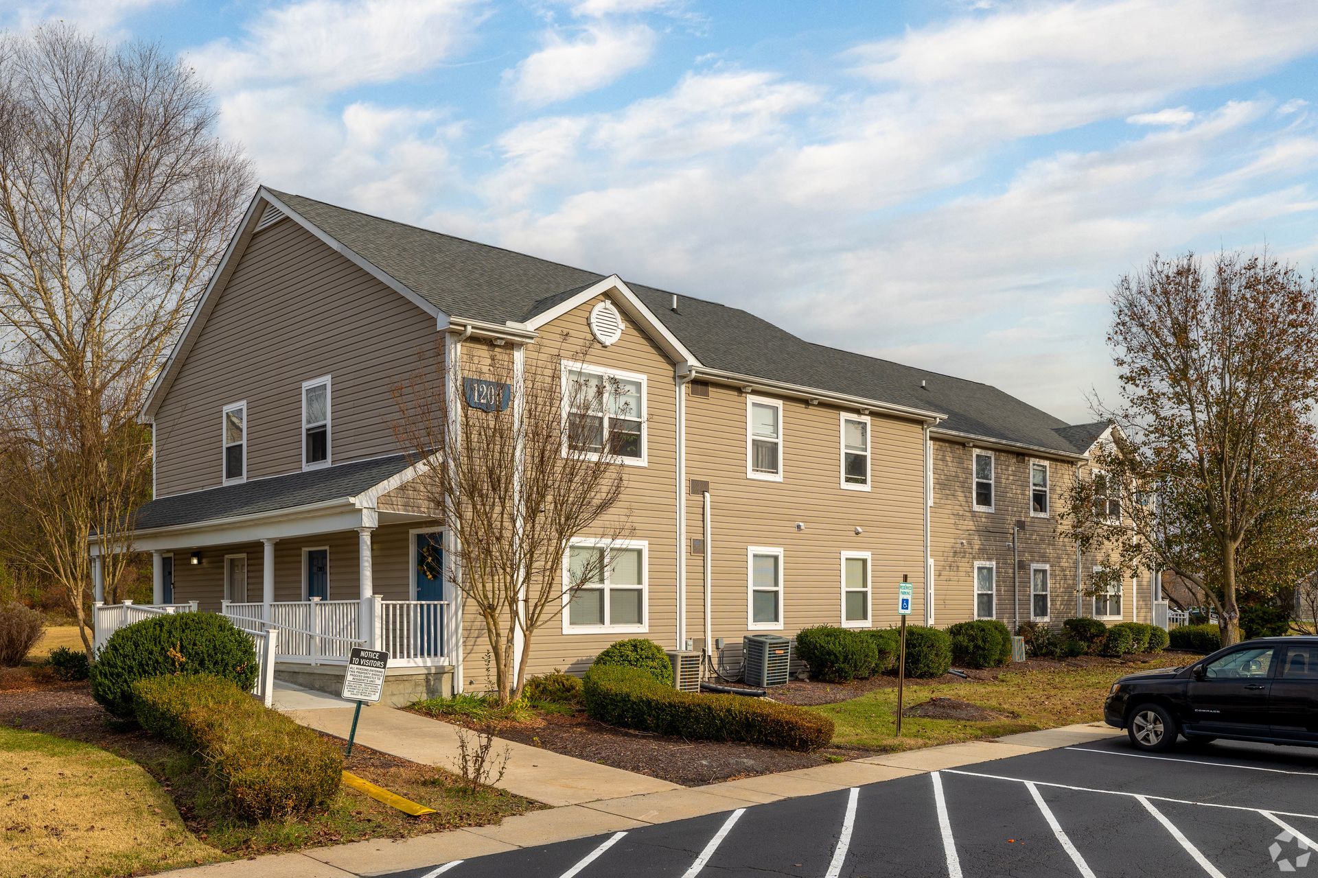 Tan apartment building with covered porch, windows, and bushes.
