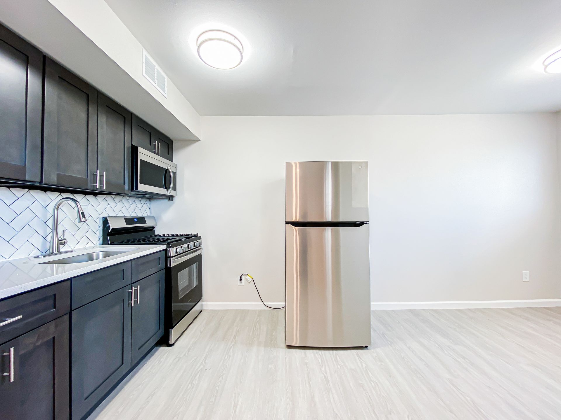 Modern kitchen with dark cabinets, stainless steel appliances, and light gray flooring.