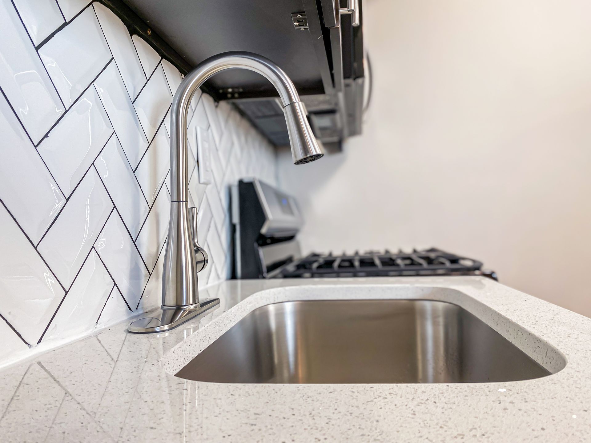 Stainless steel kitchen sink and faucet with white quartz countertop and subway tile backsplash.