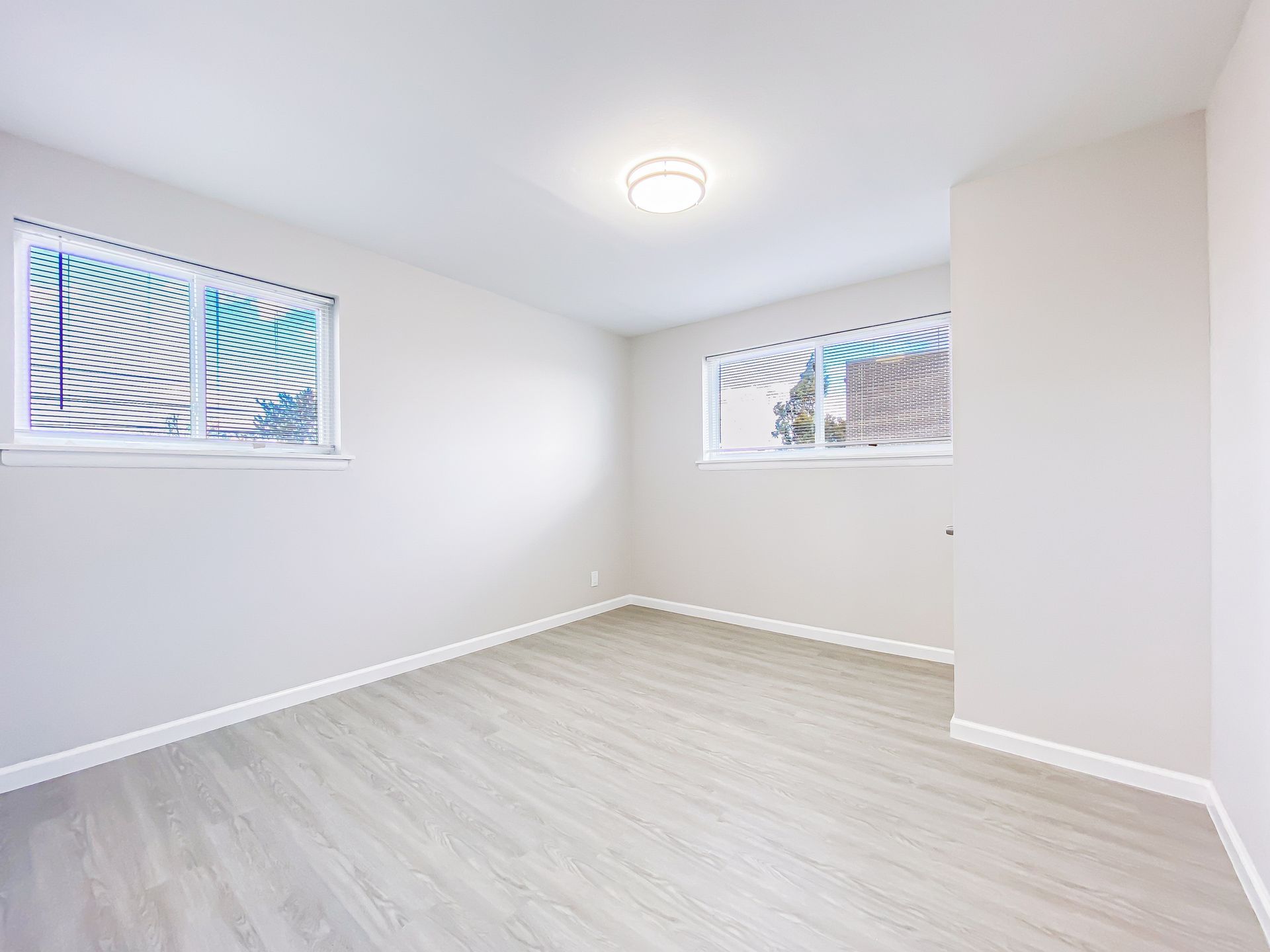 Empty room with two windows, light gray walls and flooring, ceiling light.