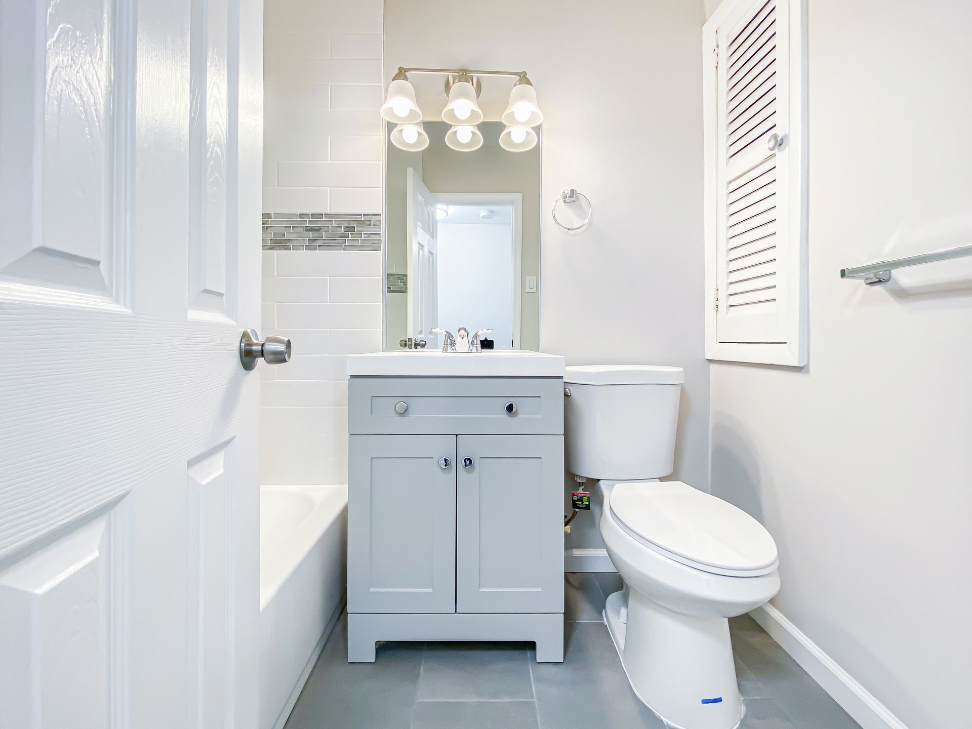 Small bathroom with gray vanity, white toilet, and tile.