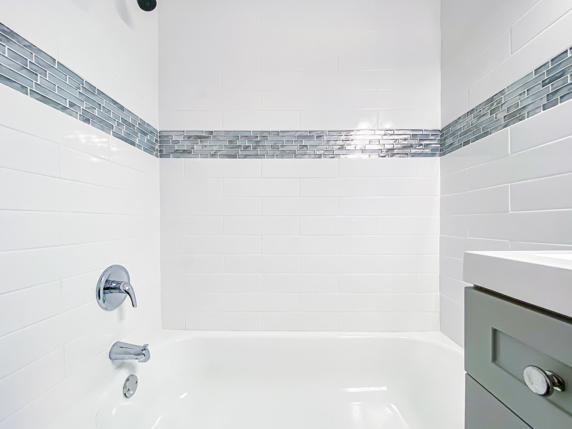 White tiled bathroom with glass tile accent, chrome fixtures, and a vanity.