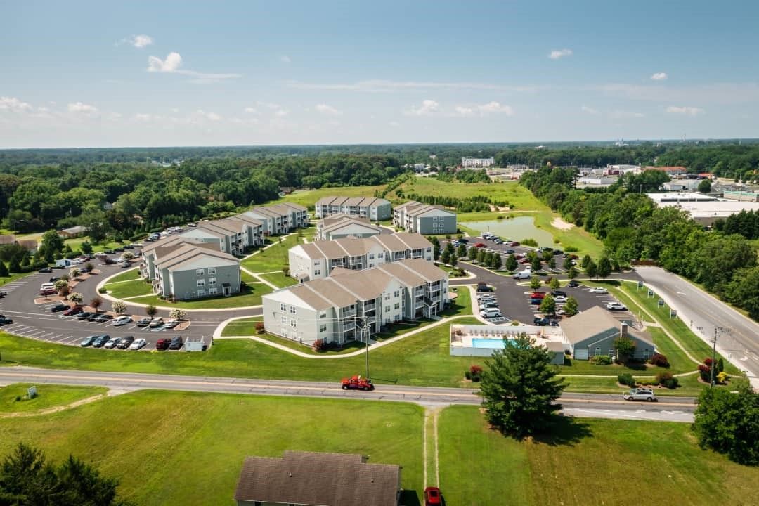 Aerial view of an apartment complex with gray buildings, green lawns, a swimming pool, and parking.