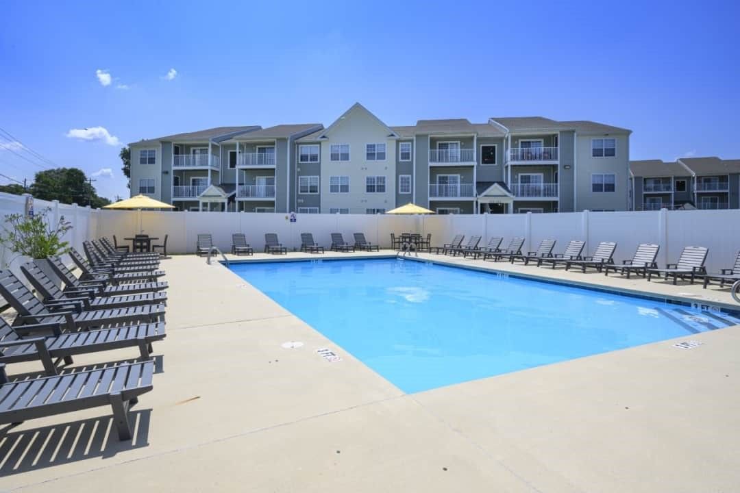 Swimming pool with lounge chairs and apartment building in the background on a sunny day.