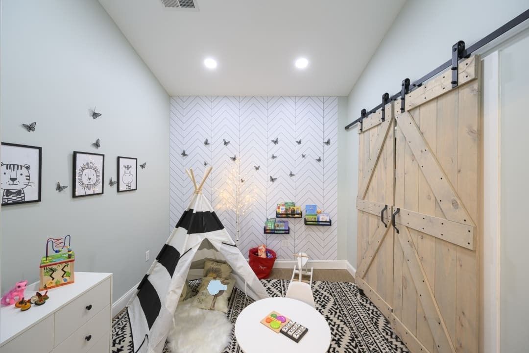 Playroom with teepee, barn door, art, and children's furniture in a light-colored room.