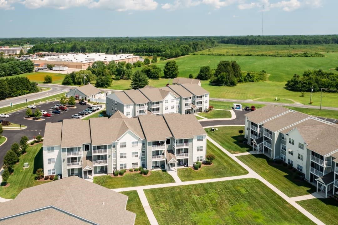 Aerial view of apartment buildings with brown roofs surrounded by green grass and trees.