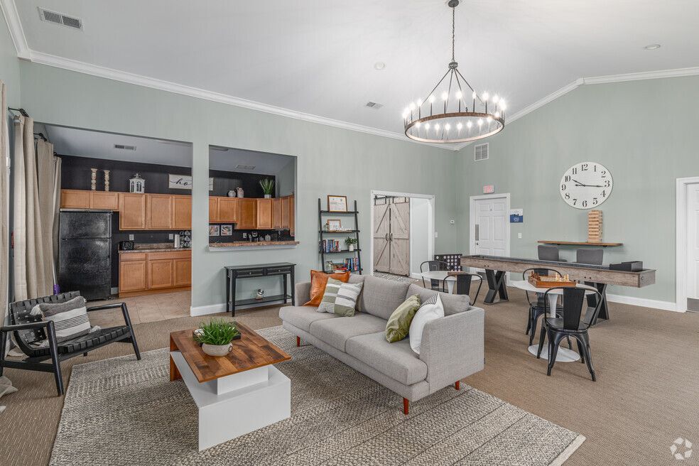 Spacious community lounge with seating, a kitchen area, and a large clock on the wall.