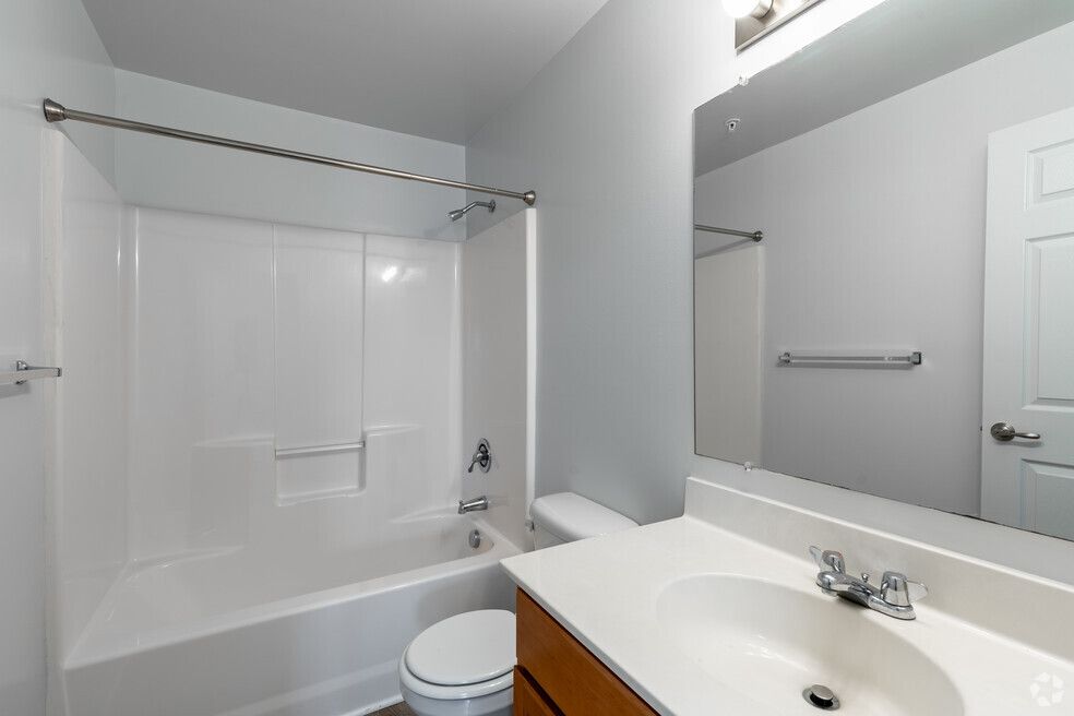 White bathroom with a tub/shower, toilet, vanity with a sink, and a large mirror.