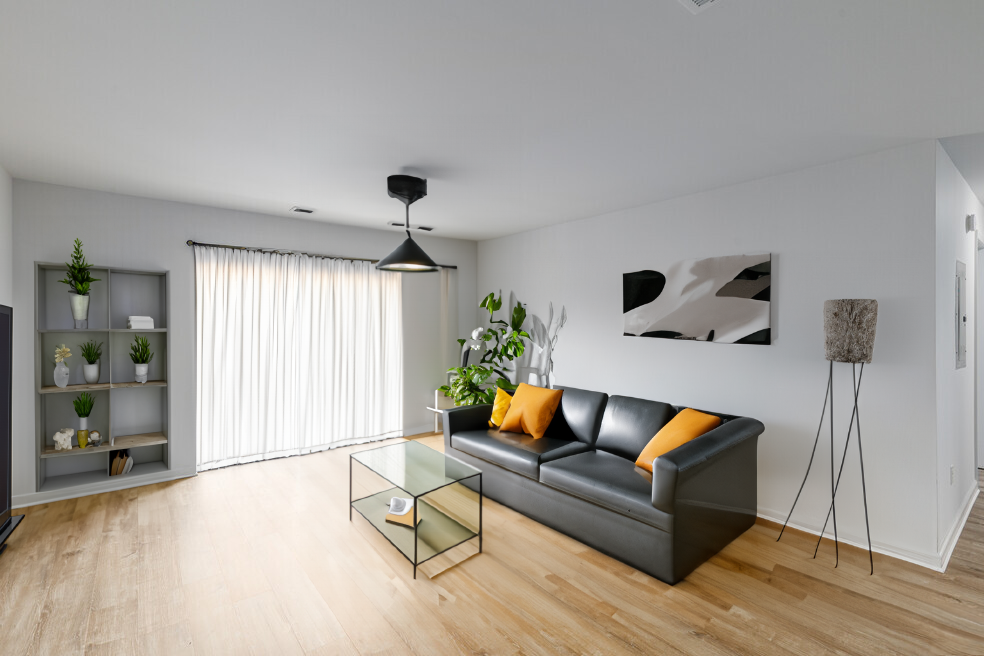 Modern living room with black leather sofa, glass table, and wooden floors.