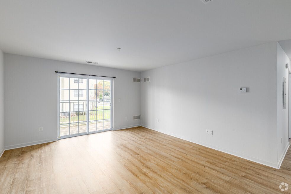 Empty living room with wood flooring, white walls, and a sliding glass door.