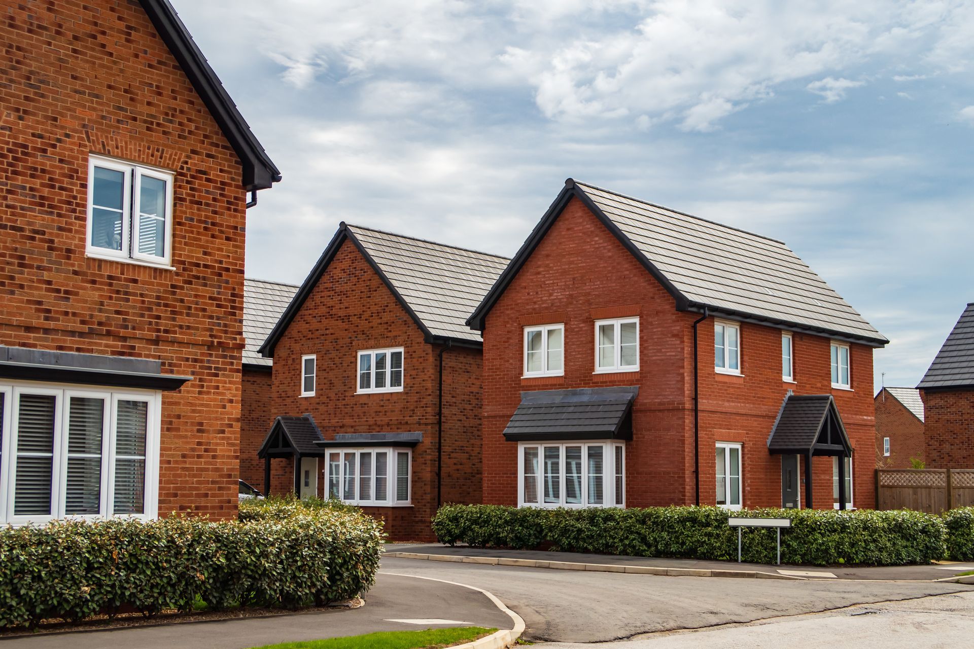 A row of red brick houses with black roofs in a residential area.