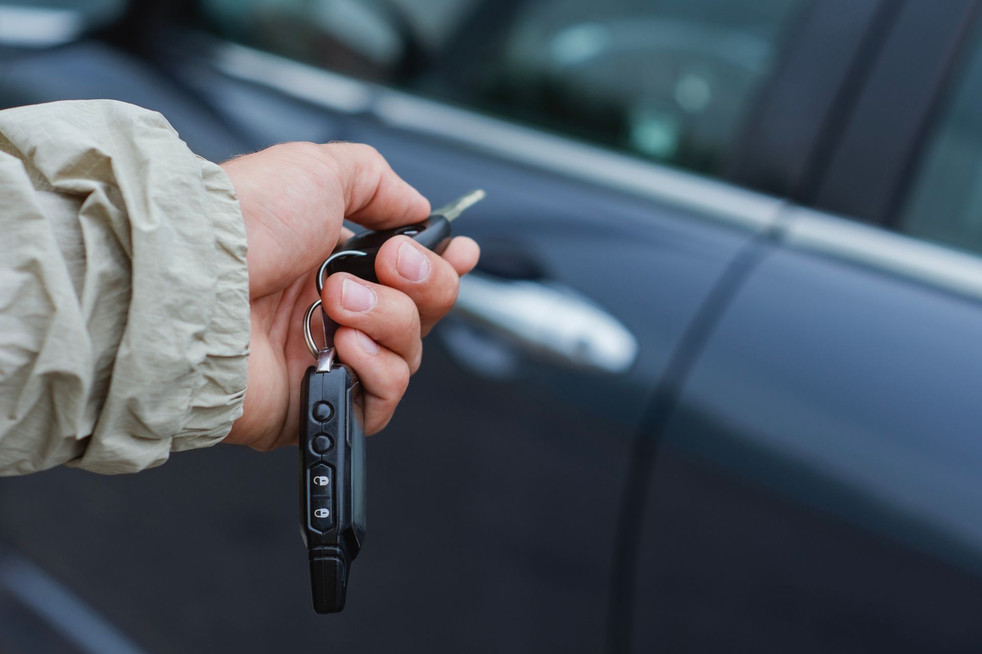 Person's hand holding car keys with a remote. The keys are near a dark blue car door.