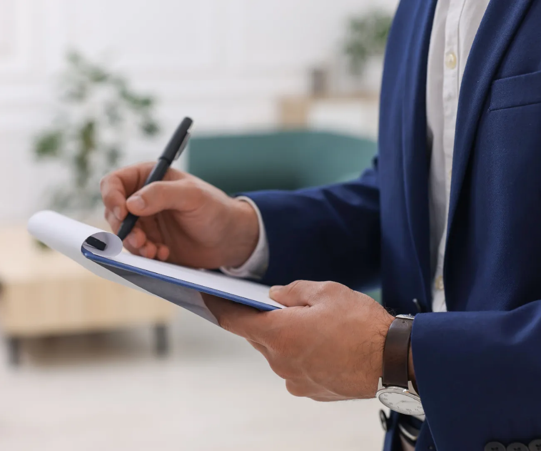 Person in a blue suit writing on a clipboard in an office setting