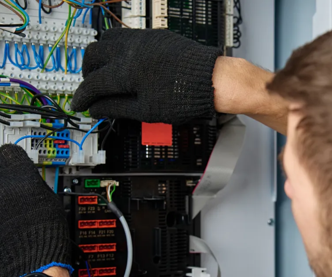 Technician wiring an electrical control panel with blue and green cables