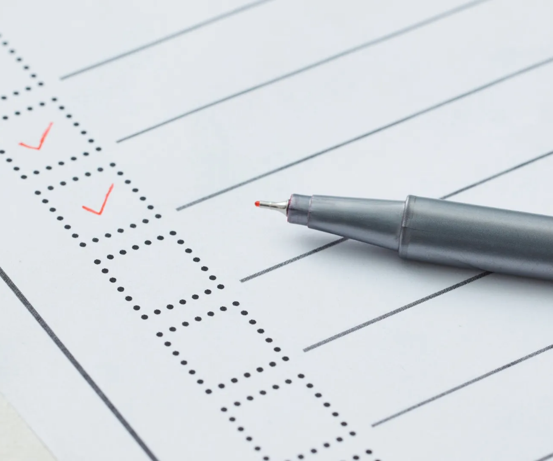 Checklist with two red check marks and a silver pen on lined paper