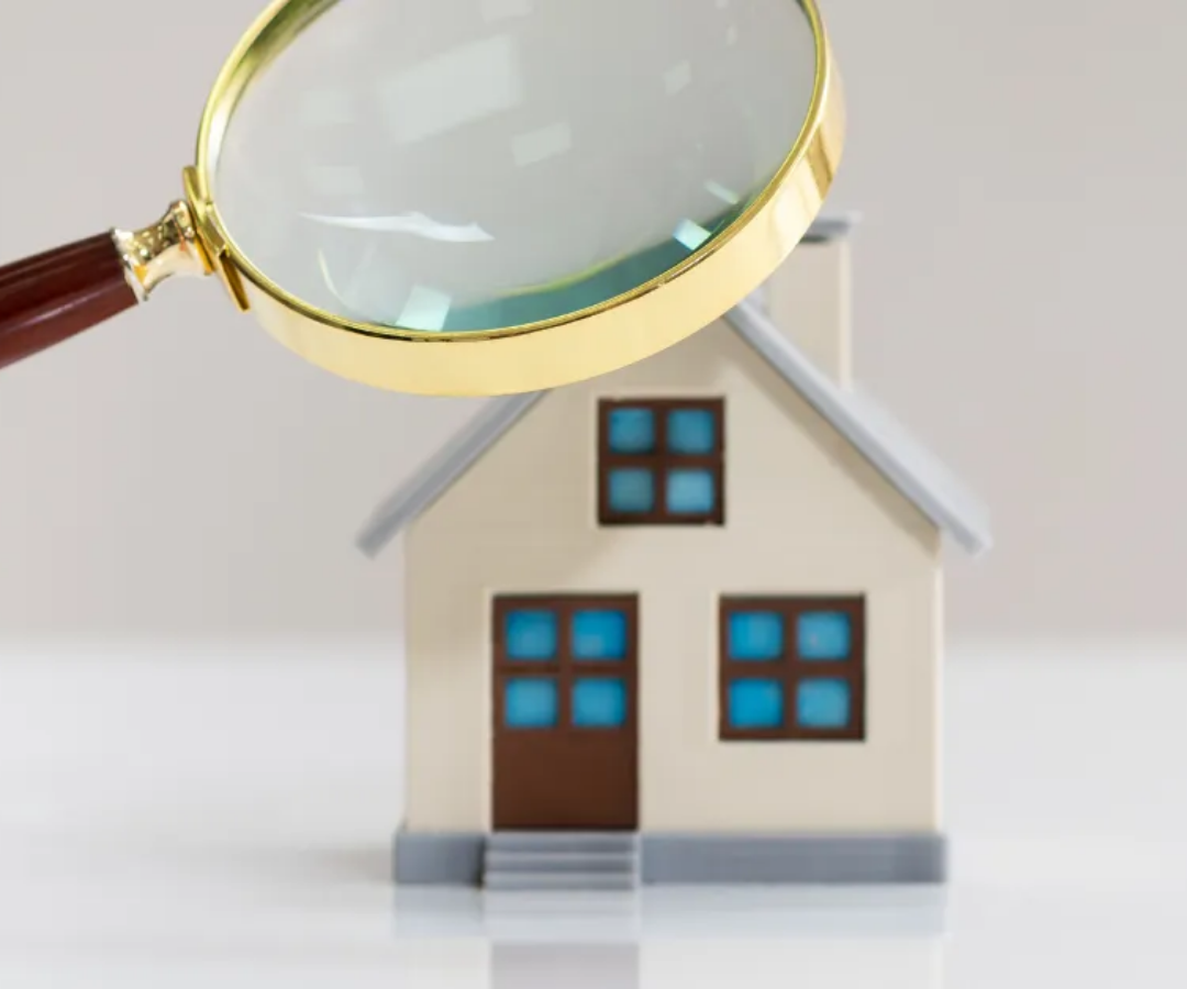 Magnifying glass over a small house model, suggesting home inspection or property search
