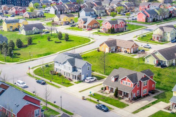 Aerial view of a colorful suburban neighborhood with houses, streets, and green lawns on a sunny day.