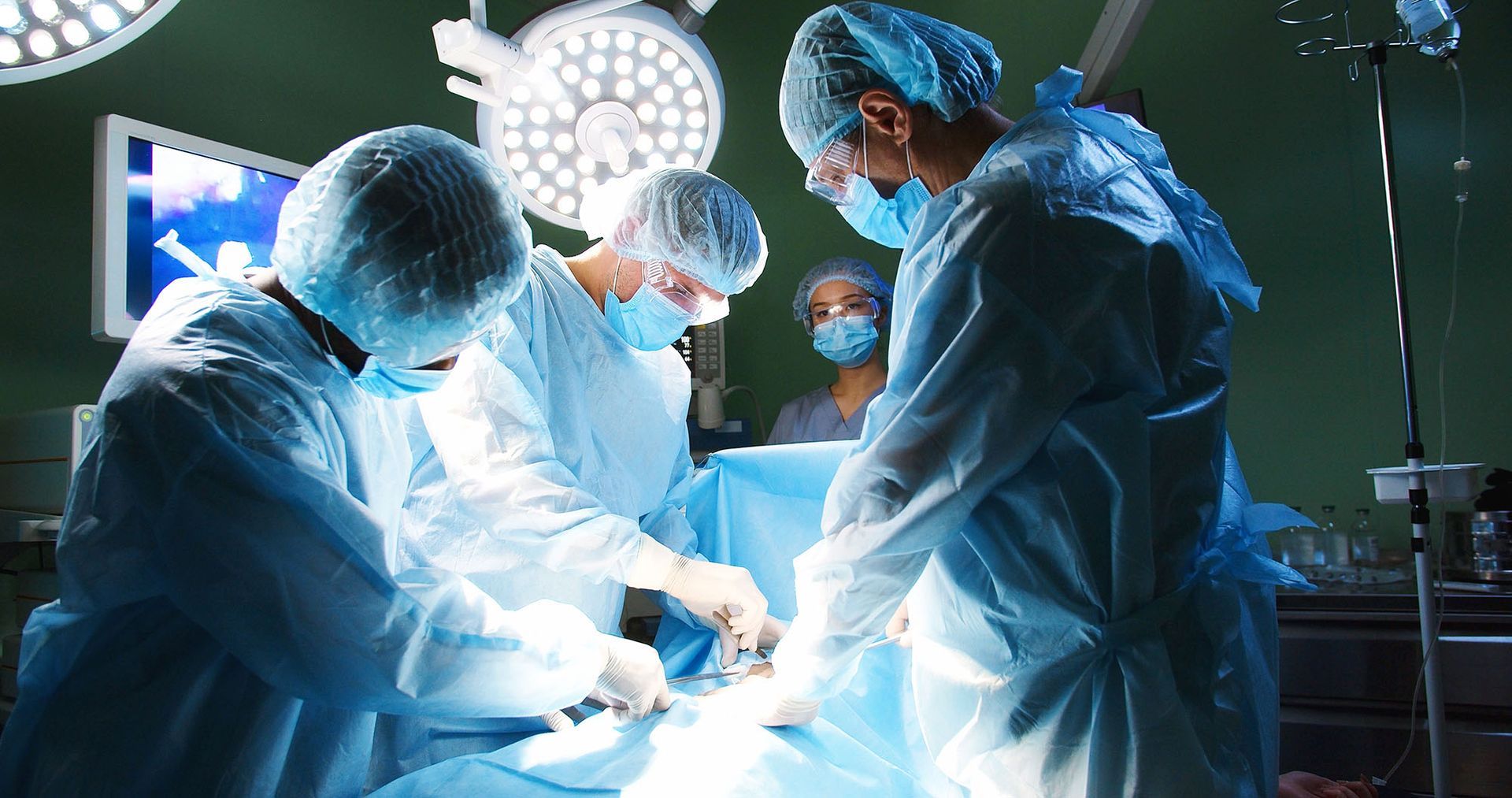 A group of doctors is performing a neurosurgery operation under bright lamps using instruments.