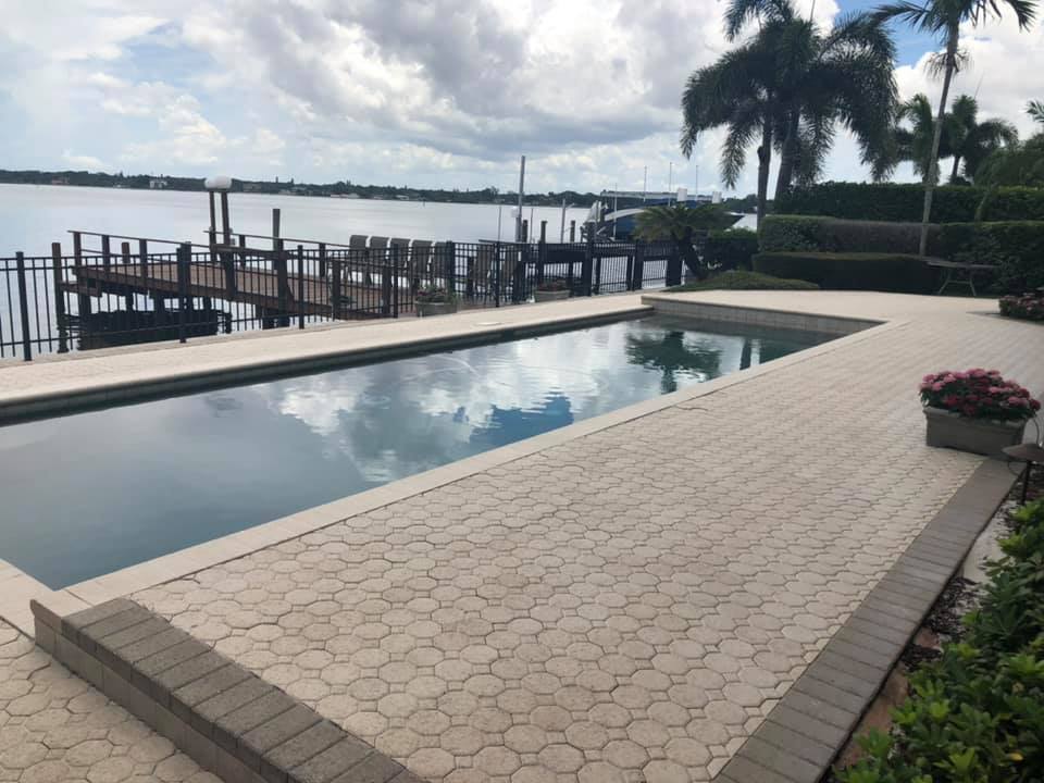Poolside view of a dock and body of water under a cloudy sky; palm trees on the right.
