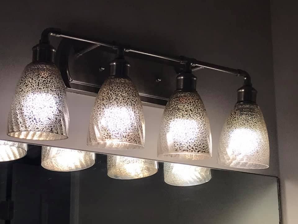 A bathroom vanity light with clear glass shades is hanging over a mirror.