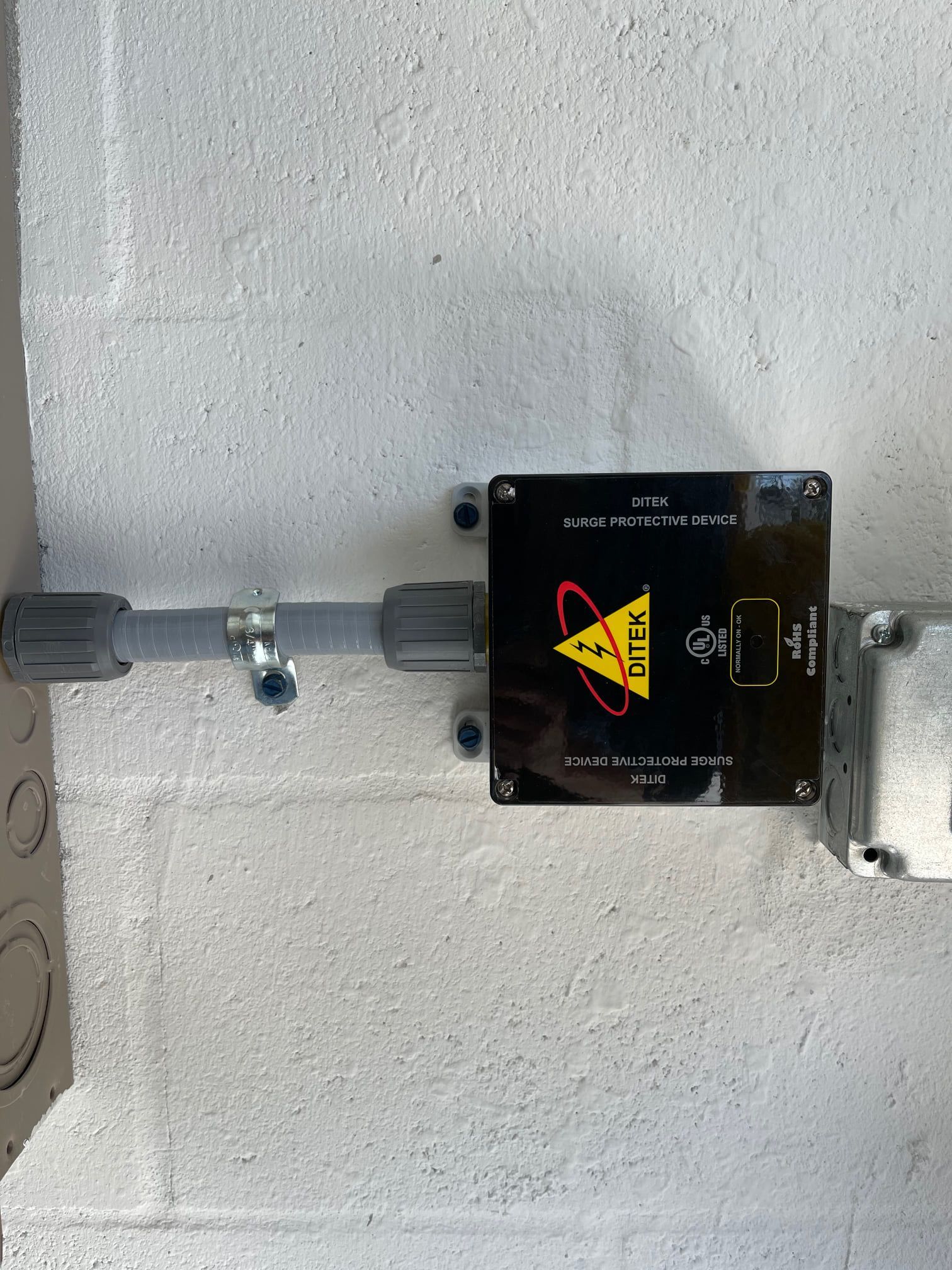 A black box with a yellow triangle on it is attached to a white wall.