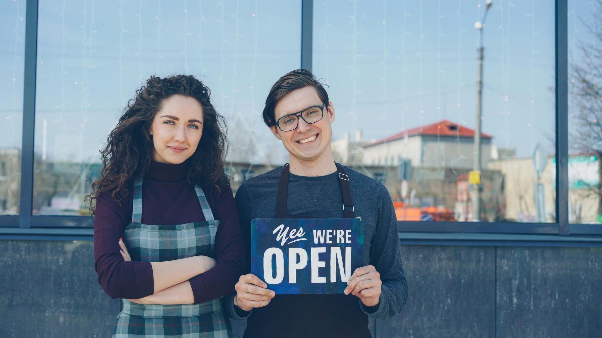 Two people standing outside, smiling at the camera and holding a sign that says 