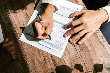 Hands filling out a document with a pen on a wooden table.