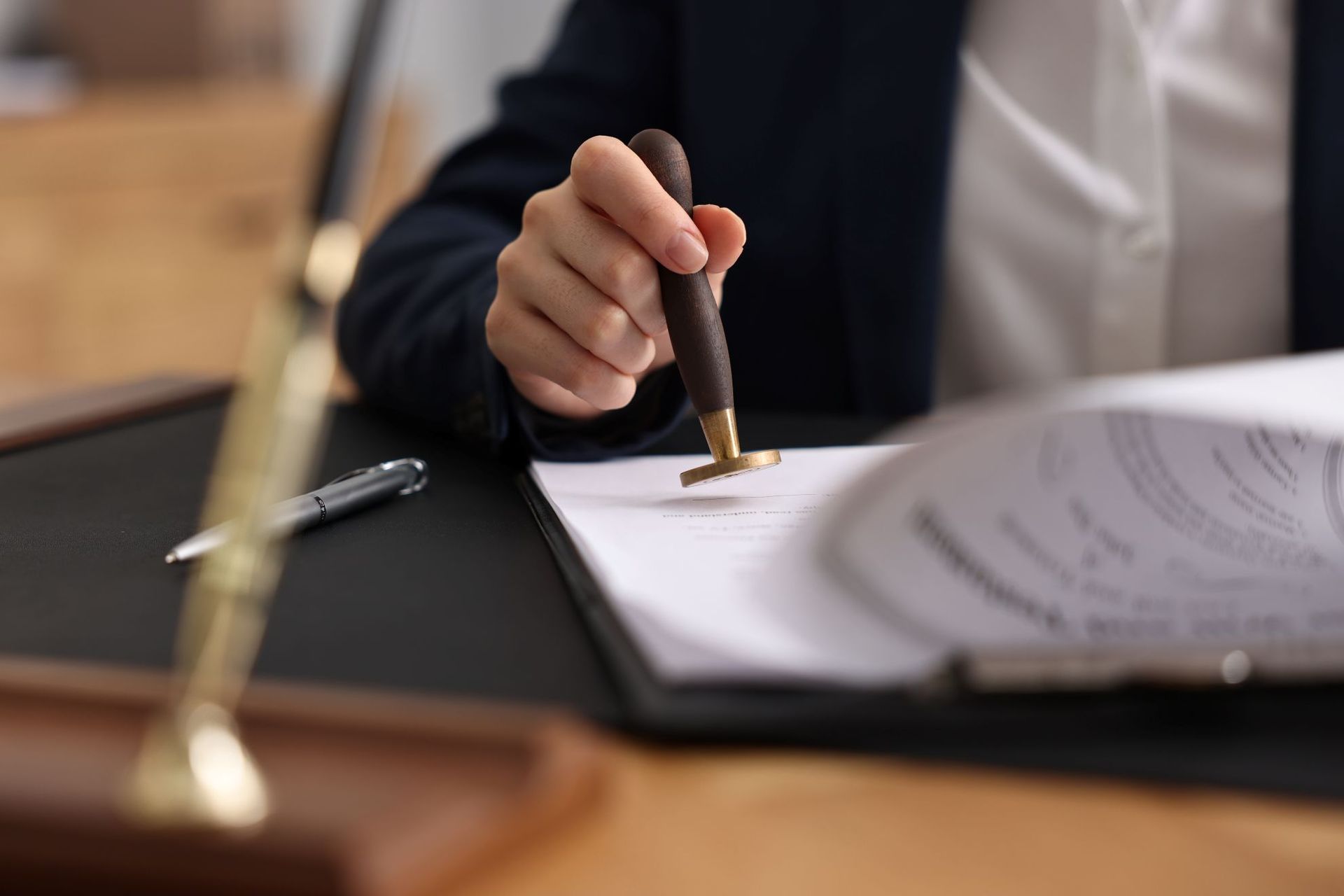 A person in a dark suit using a wax seal stamp on a document at a desk with a pen nearby.