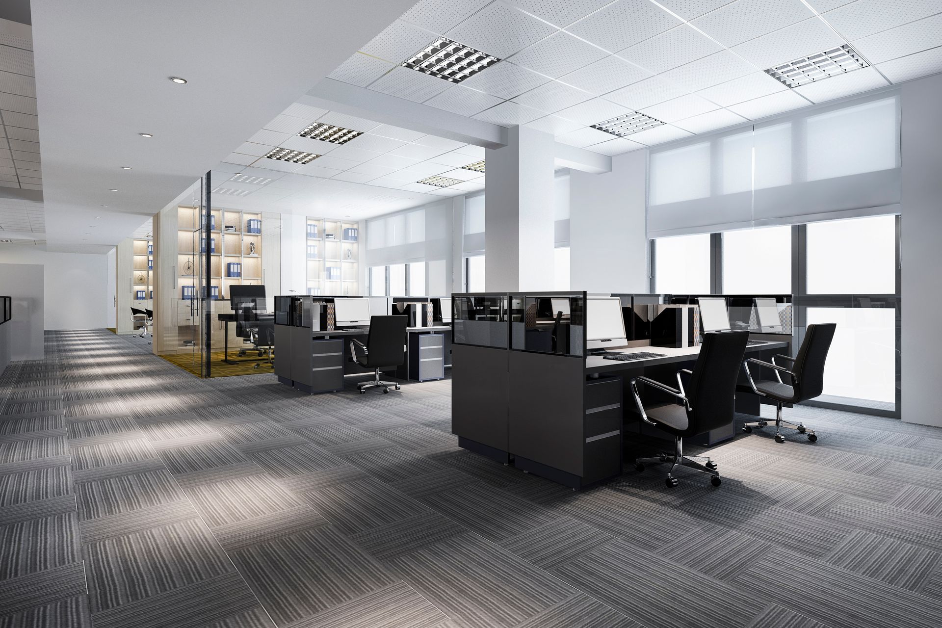 Modern open-plan office with desks, chairs, large windows, and gray carpet under bright ceiling lights