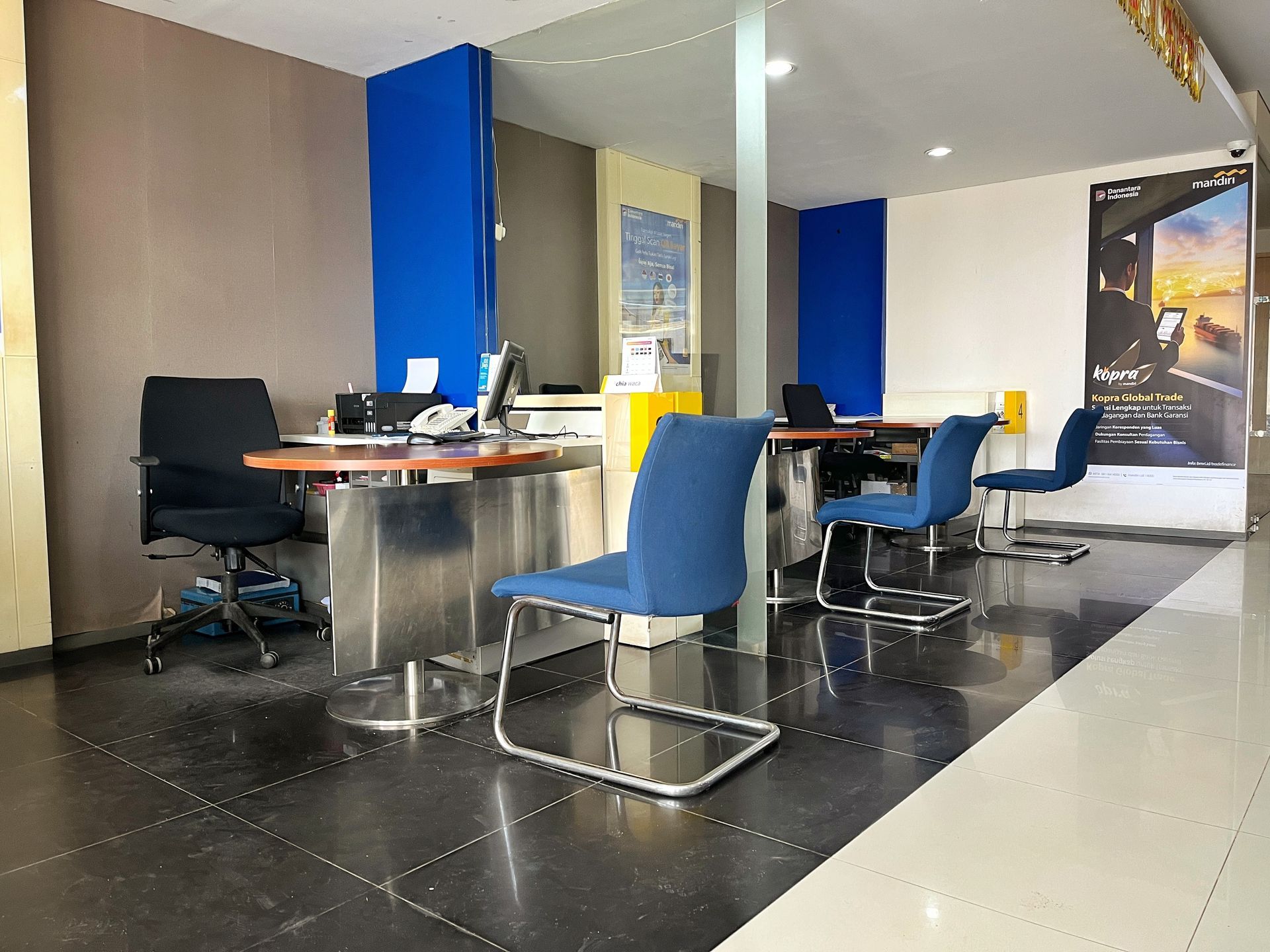 Office waiting area with blue and black chairs, tables, and a glossy tiled floor