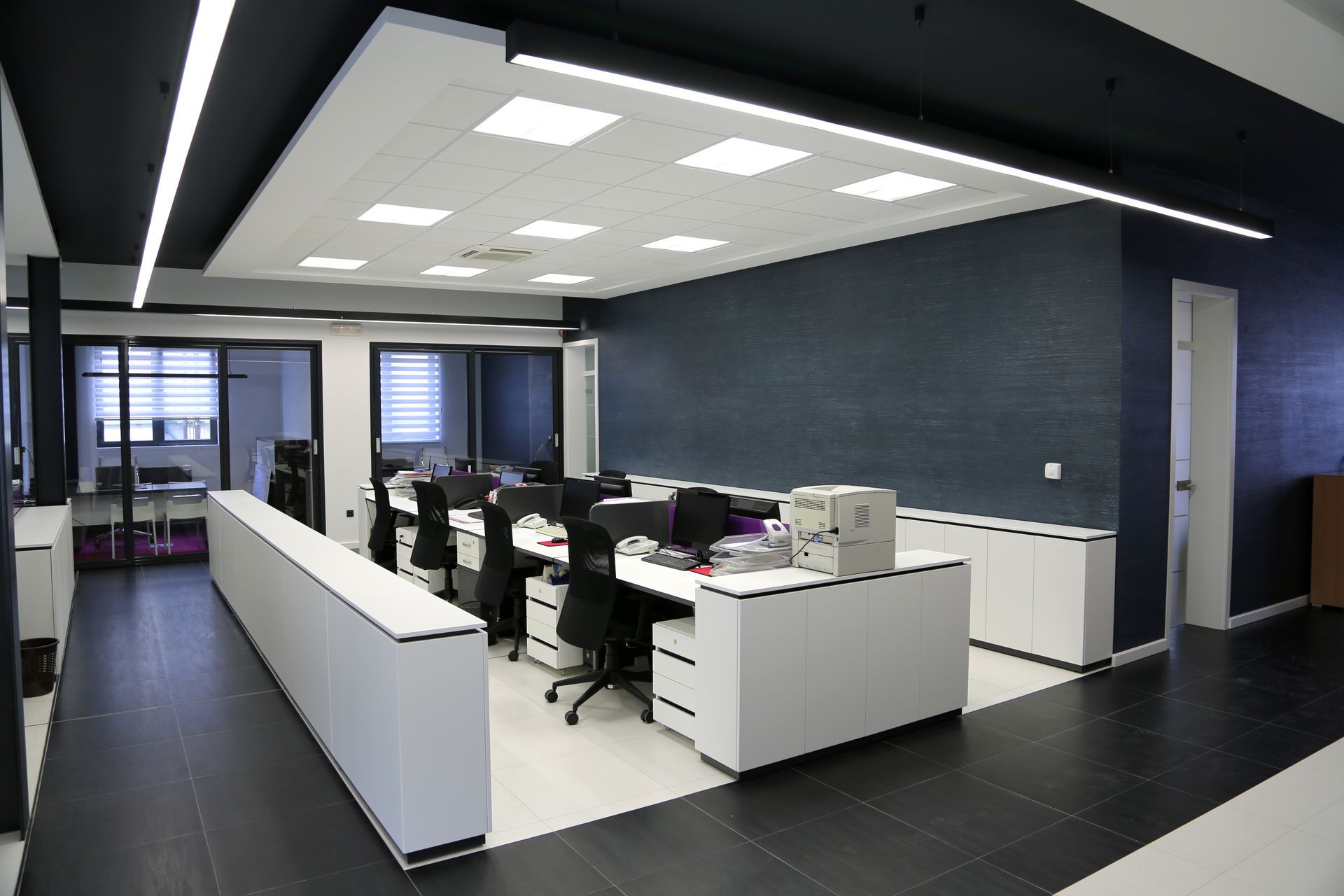 Modern office interior with desks, computers, and dark gray walls under bright ceiling lights
