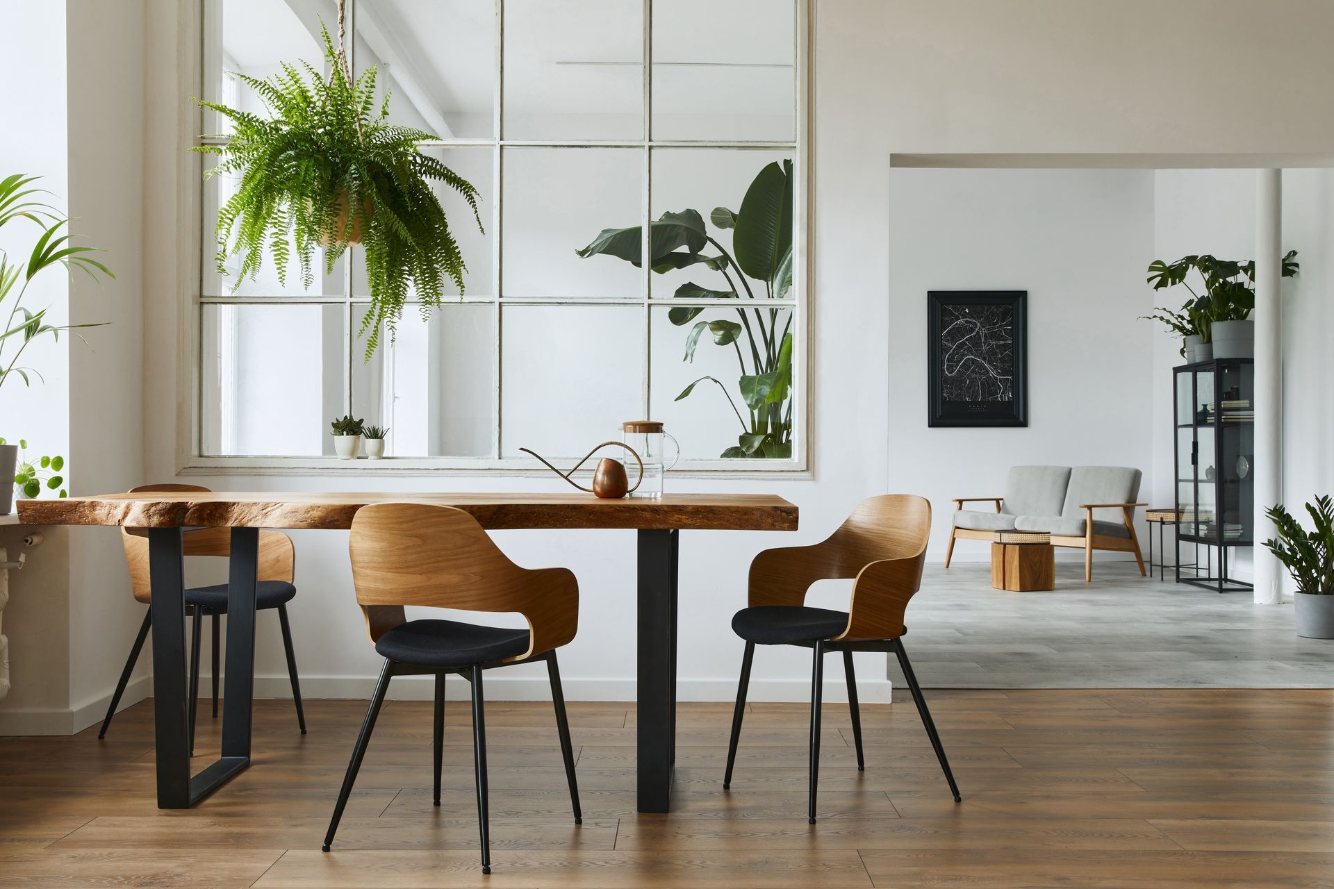 Modern dining area with wooden table, black chairs, and hanging plants by large windows