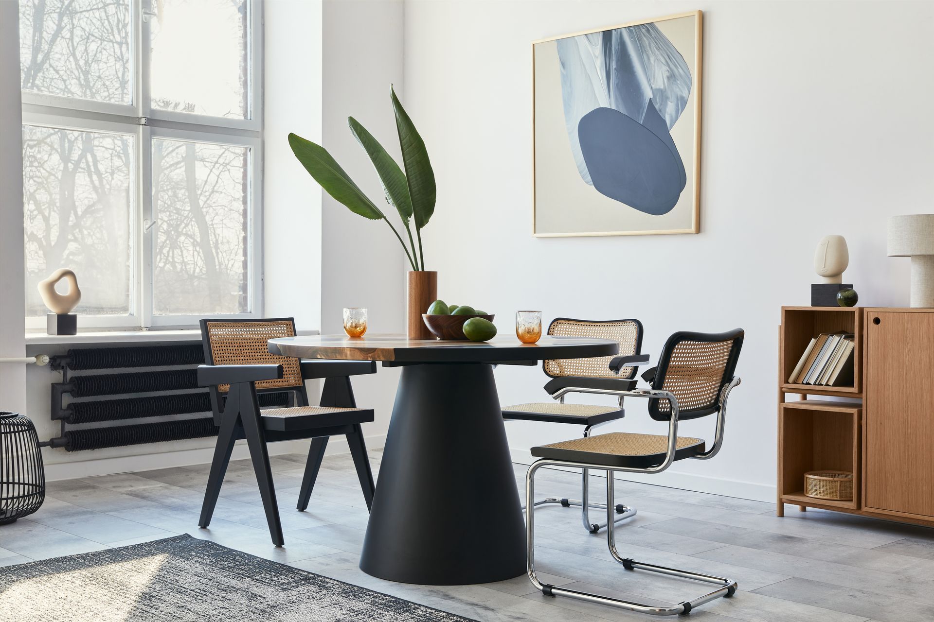 Modern office with black desk, chairs, wooden cabinet, large window, plant, and abstract wall art.