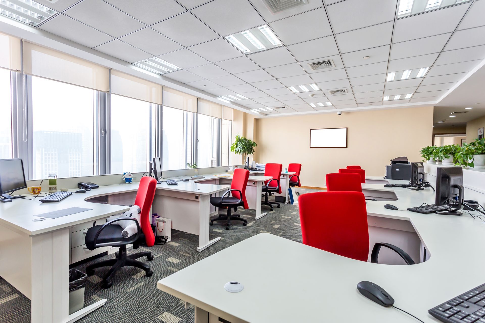 Bright modern office with white desks, red chairs, computer monitors, and large windows