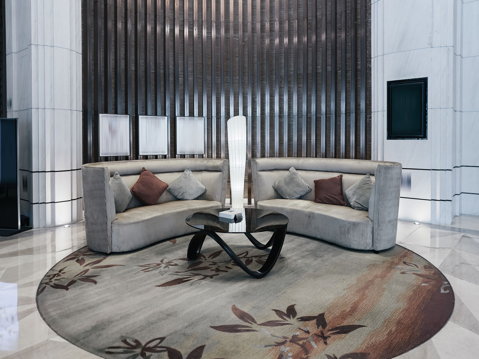 Modern lobby with two gray sofas, round floral rug, and black glass coffee table in a sleek interior