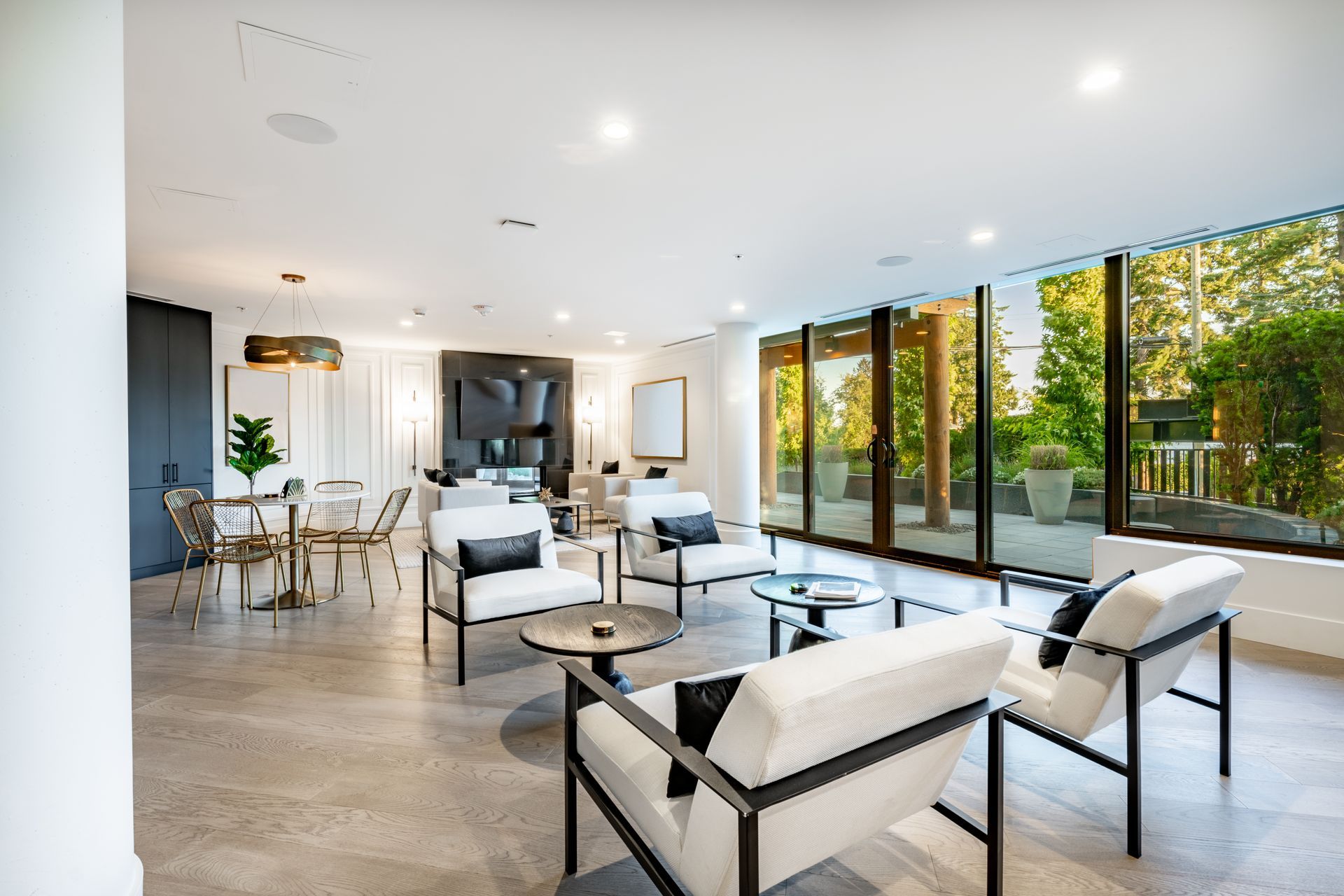 Modern living room with white chairs, glass coffee tables, and floor-to-ceiling windows overlooking greenery