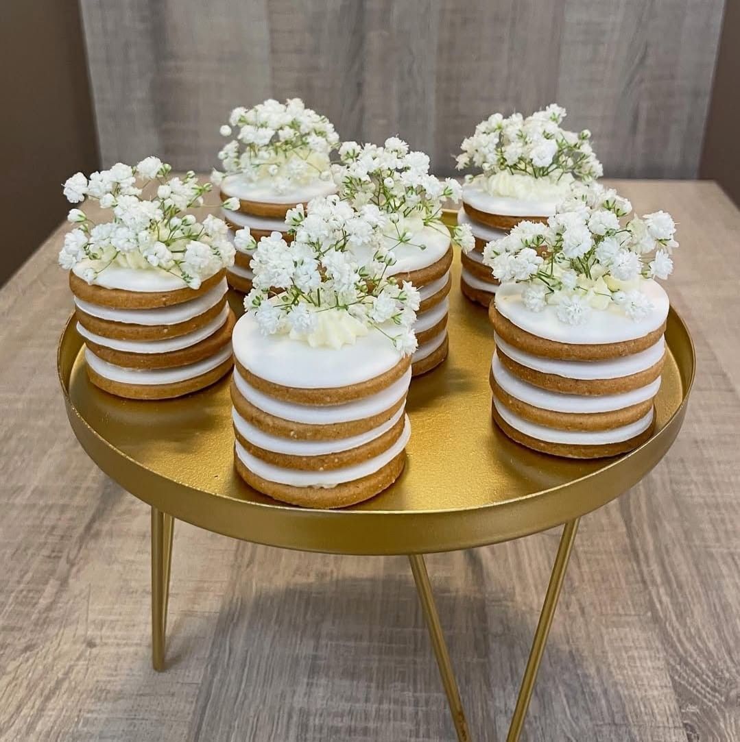 Mini torte con glassa bianca e fiori di gypsophila, impilate su un'alzata dorata.
