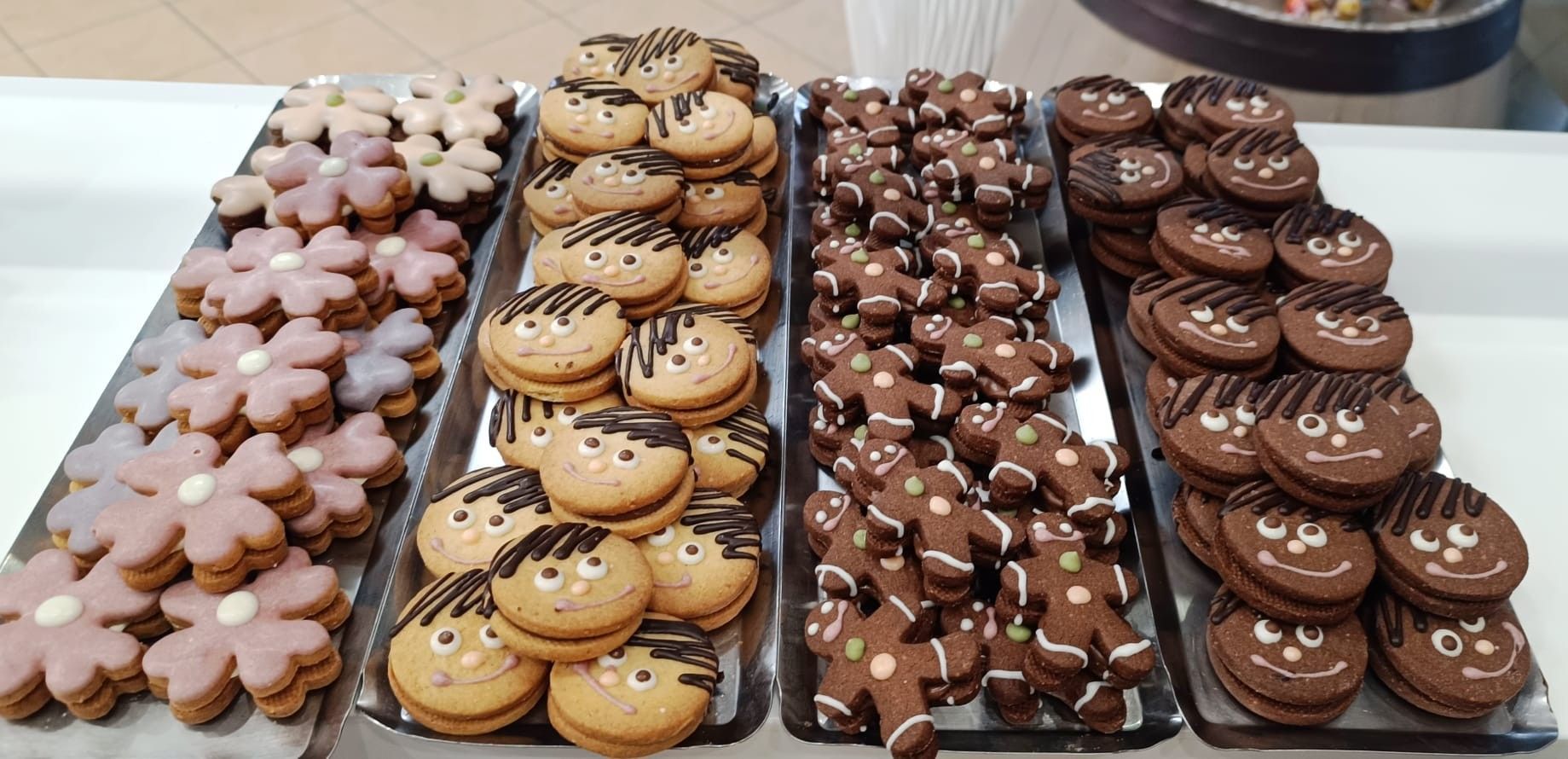 Esposizione di vari biscotti su vassoi, tra cui quelli a forma di fiore, a forma di viso e a forma di omino di pan di zenzero.