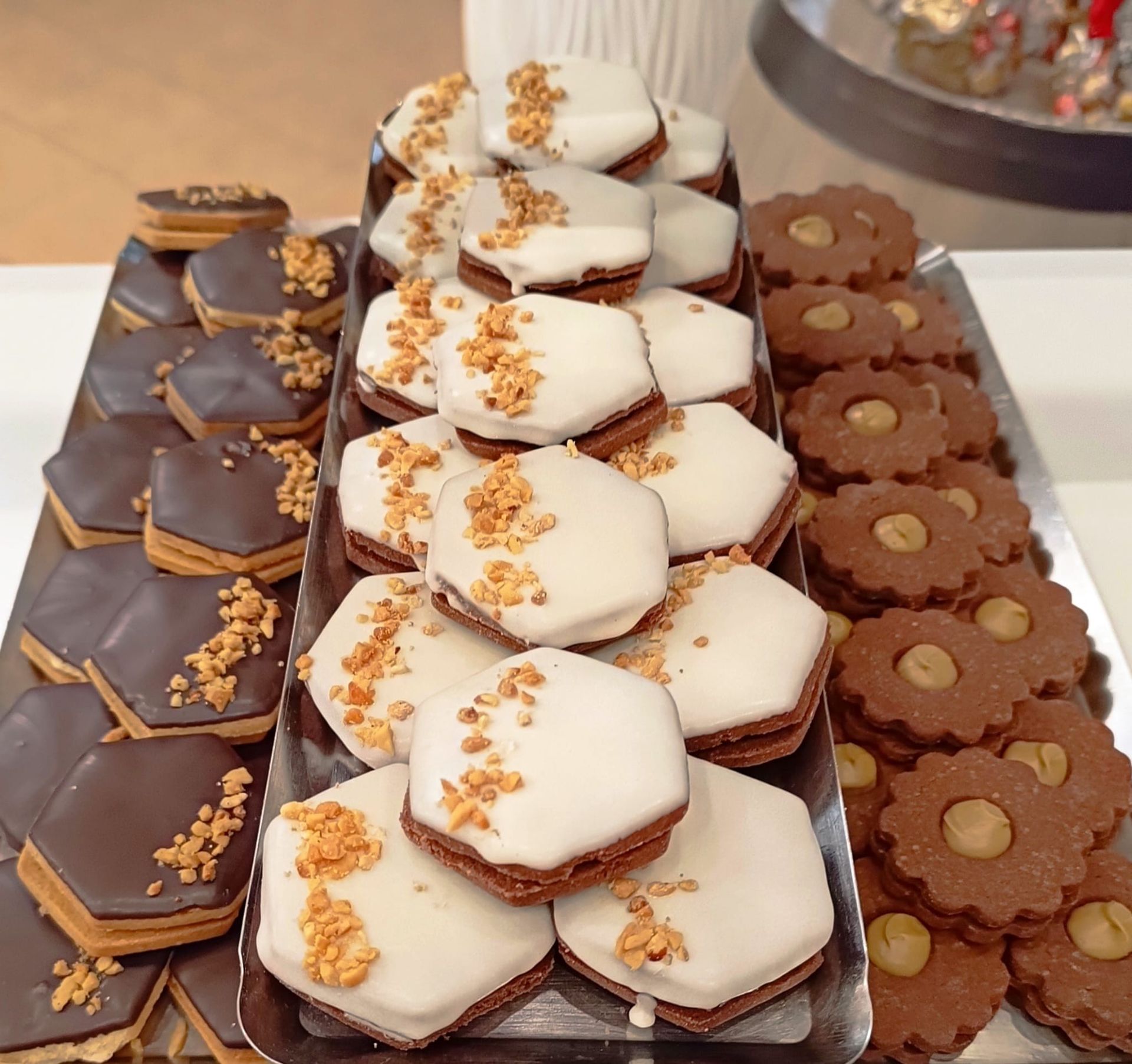Vassoio di biscotti decorati in vari modi: esagoni ricoperti di cioccolato, biscotti glassati e biscotti rotondi ricoperti di nocciole.